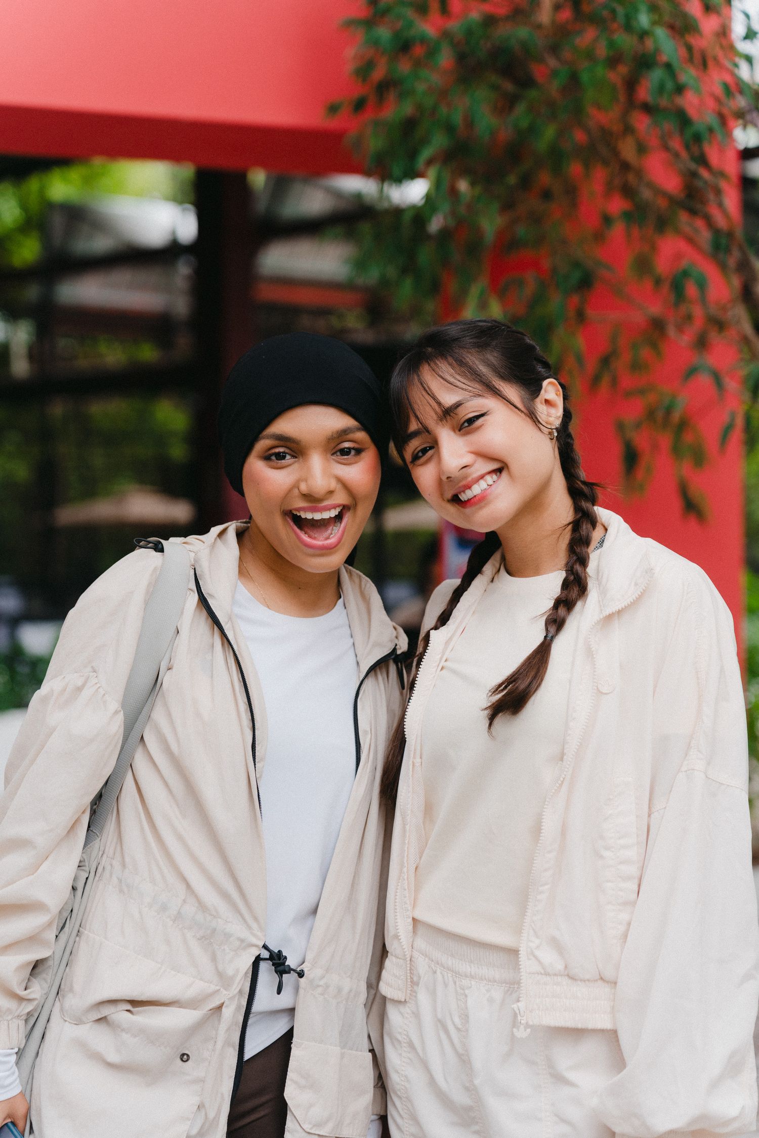 Two people in white jackets share a joyful moment together under green foliage outdoors.