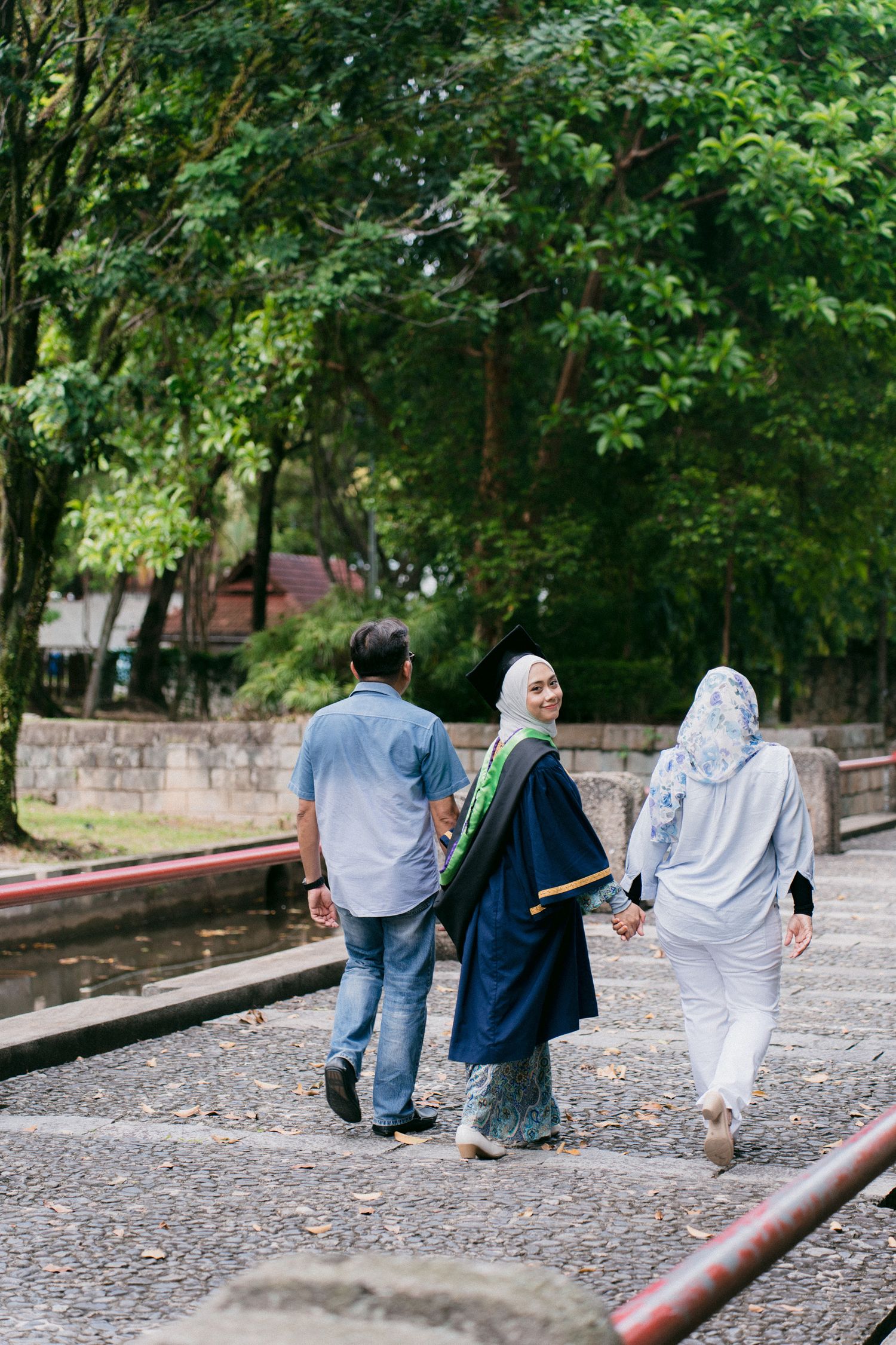 People walking together on a cobblestone path through a lush green park area with trees in the background.