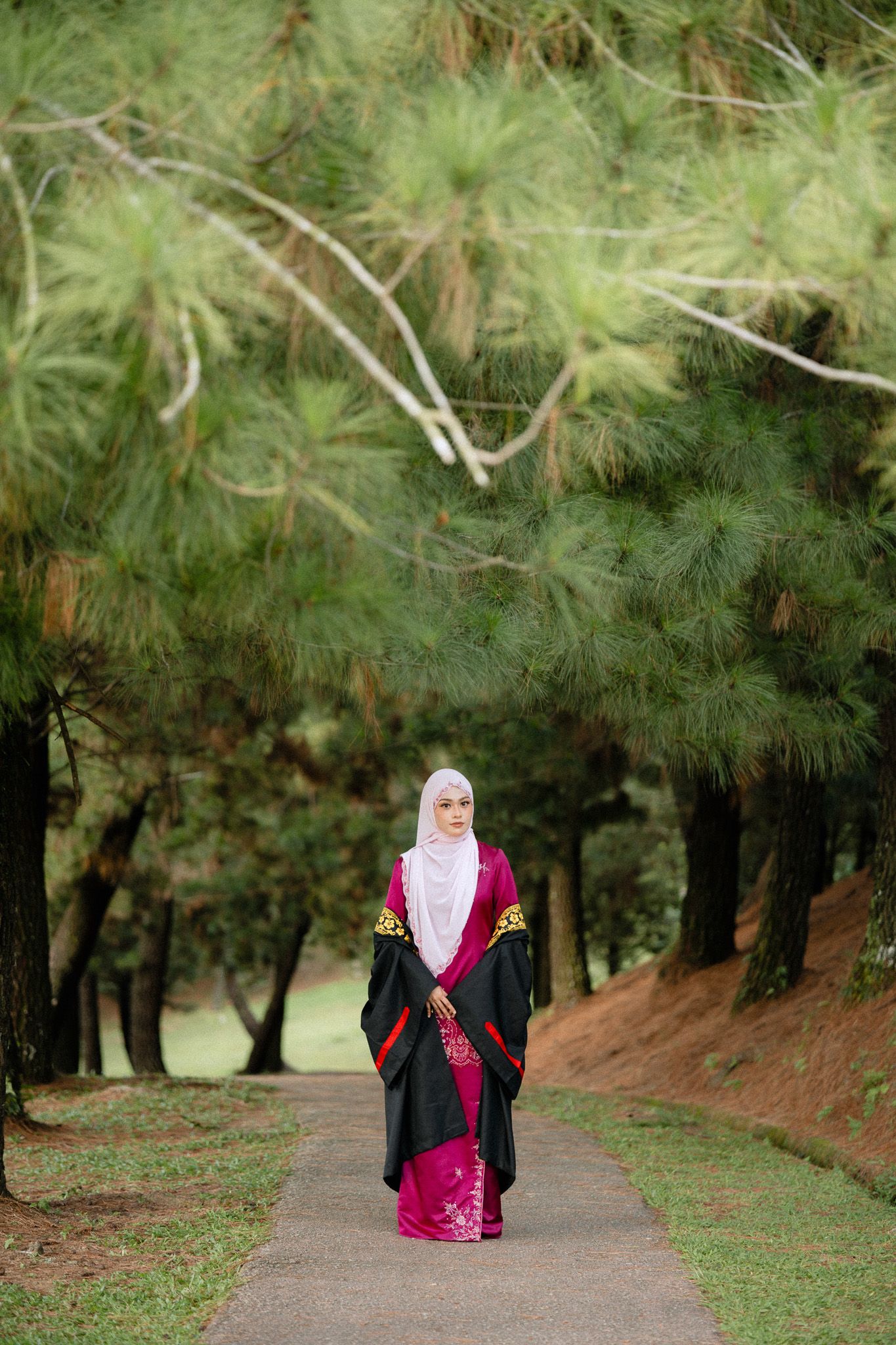 Muslim woman in hijab and black robe walks along a tree-lined path in a lush green park.