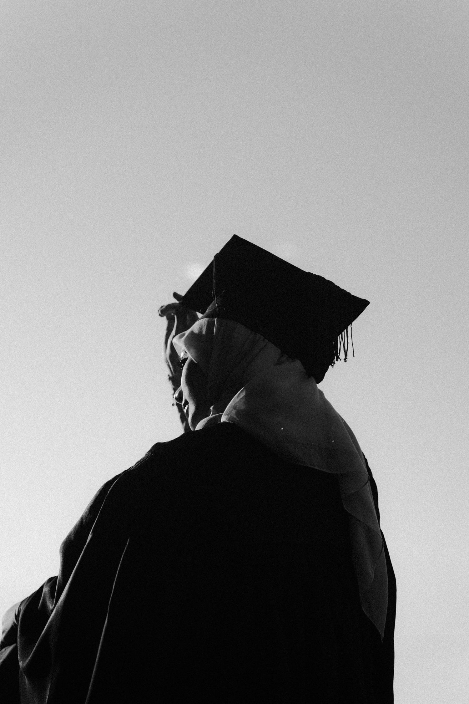 Black and white silhouette of graduates wearing mortarboard caps against a light background.