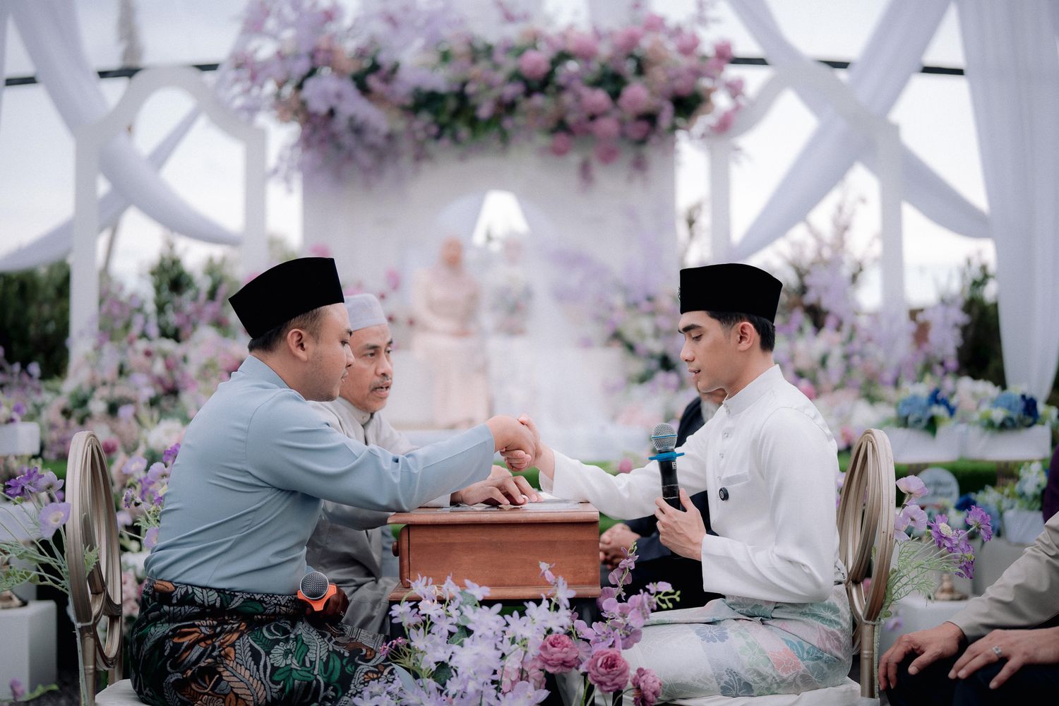 Traditional Malay wedding ceremony with two men in baju melayu and songkok performing akad nikah ritual.
