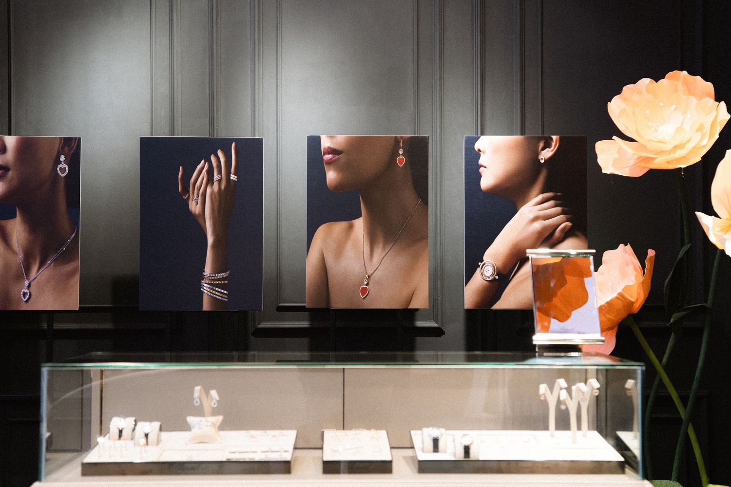 Jewelry display with marketing photos and orange flowers in an elegant retail setting.