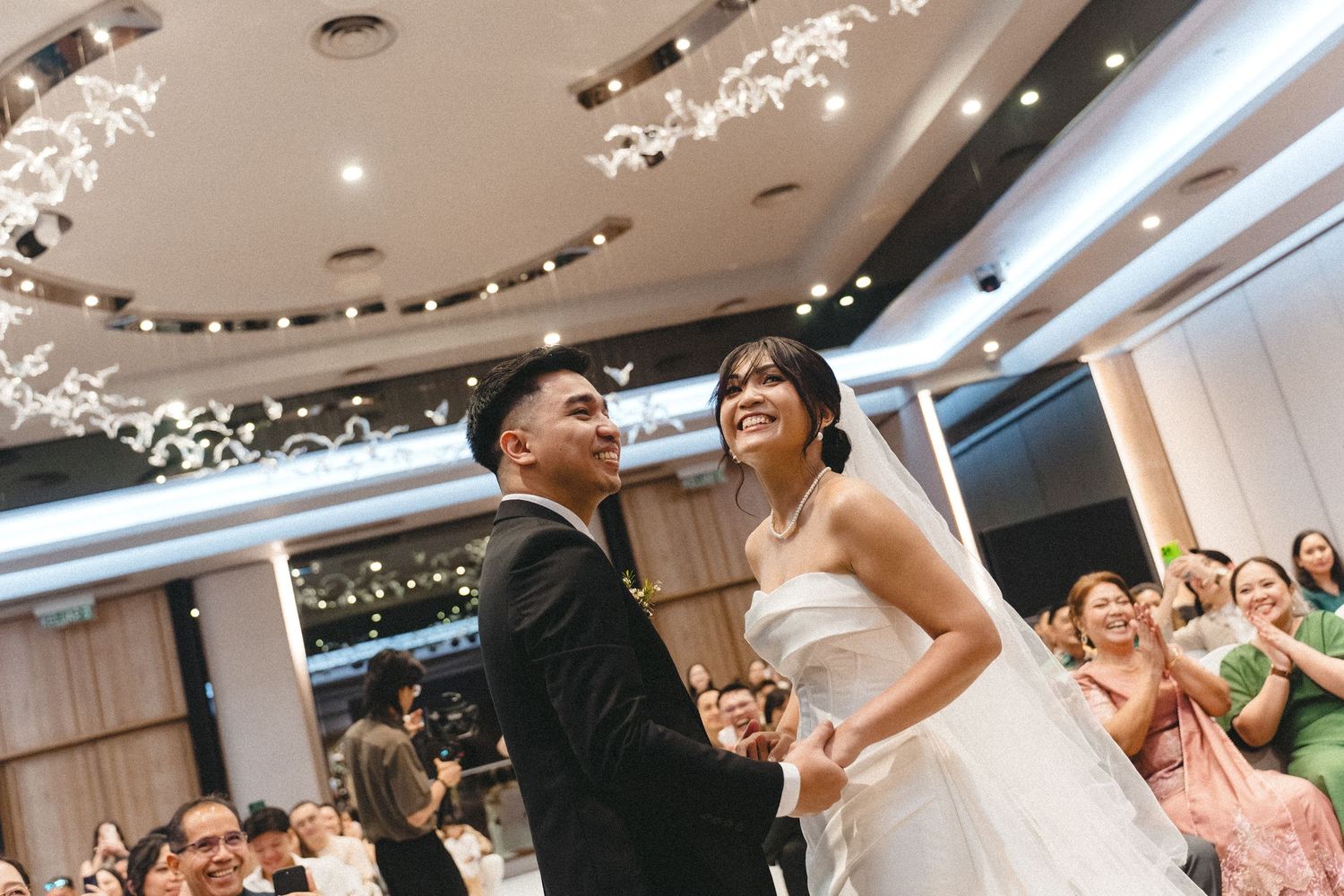 Couple shares a joyful moment on the dance floor at their wedding reception while guests cheer in the background.