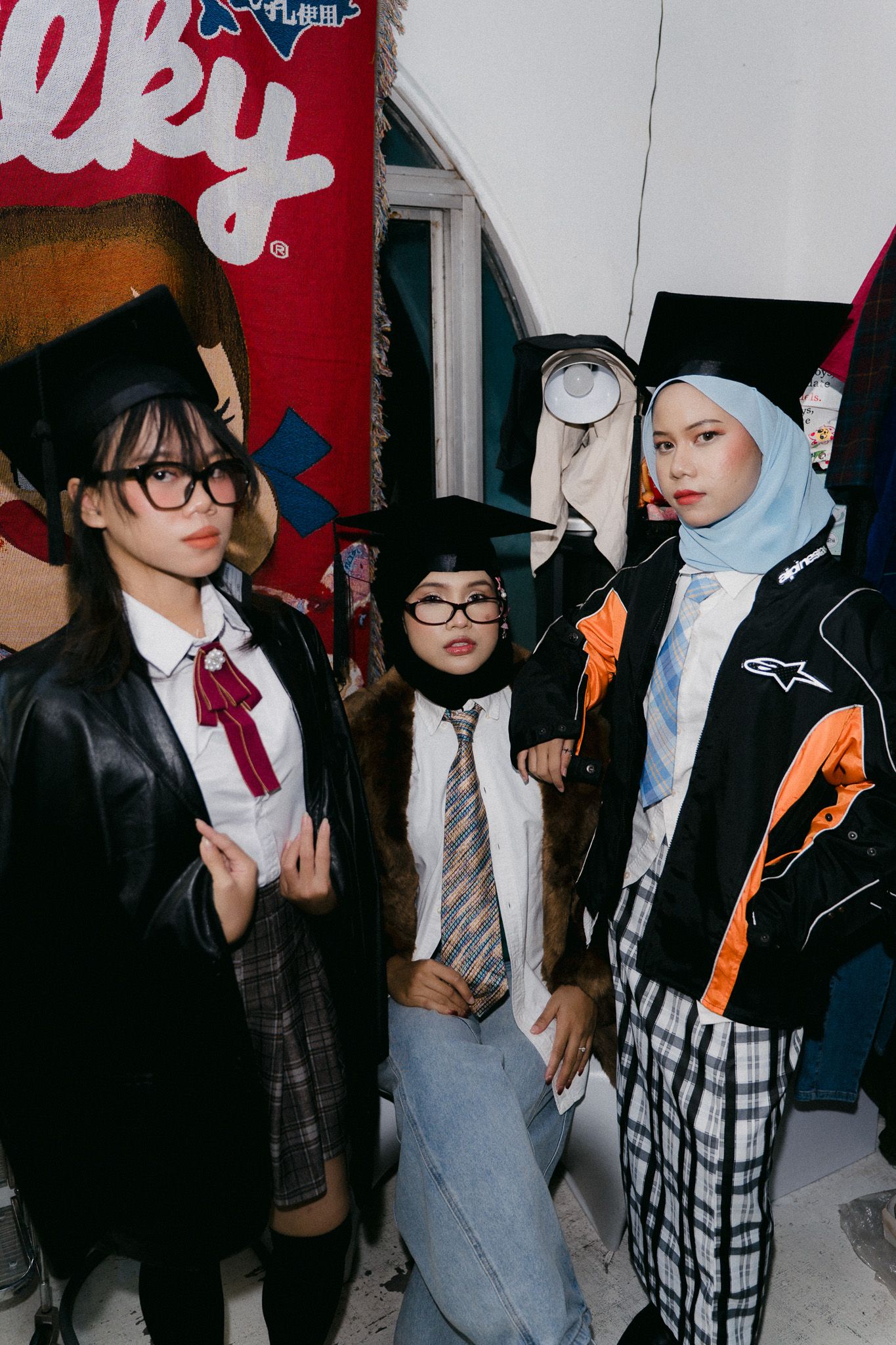 Three young people wearing graduation caps and costumes pose together indoors near colorful banners.