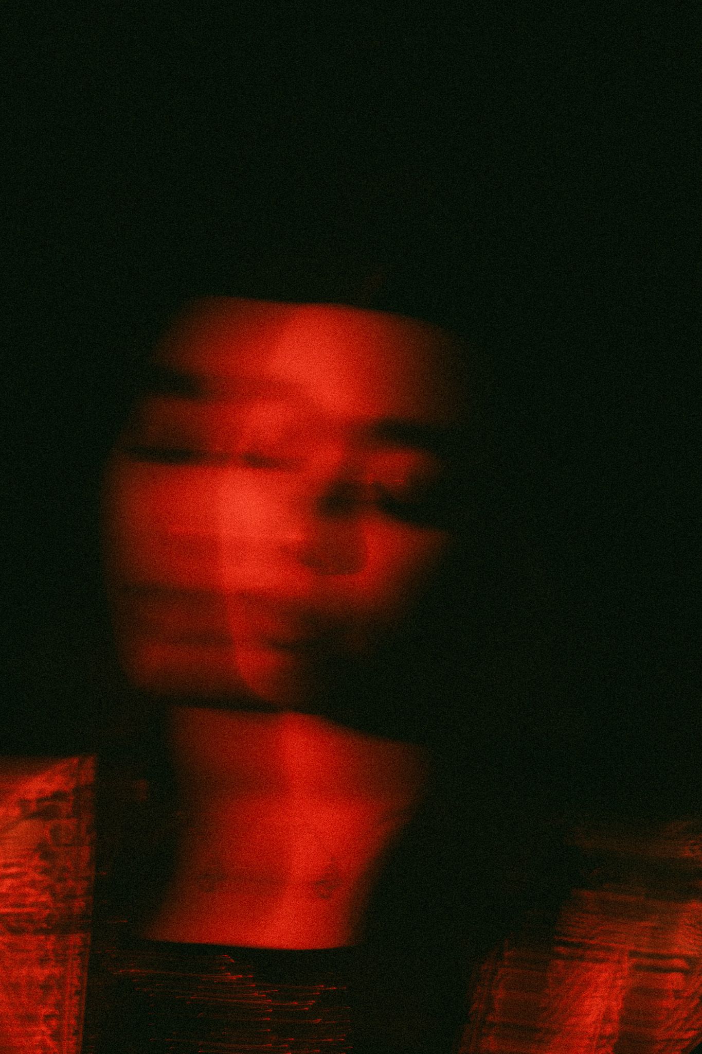 Blurry motion portrait of a person bathed in dramatic red light against a dark black background.
