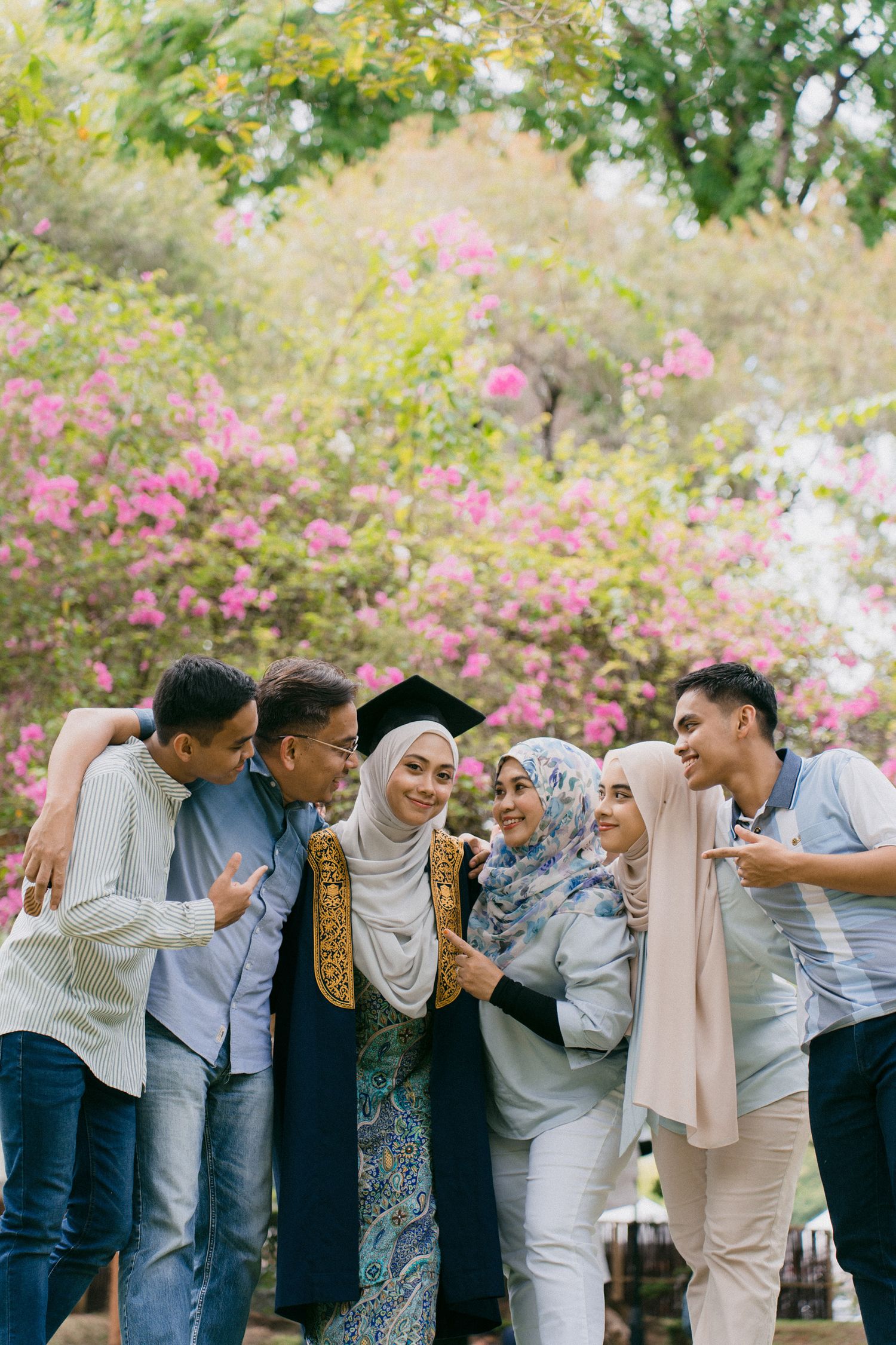 A group of friends in casual attire laughing and enjoying a moment together outdoors with pink flowers in the background.
