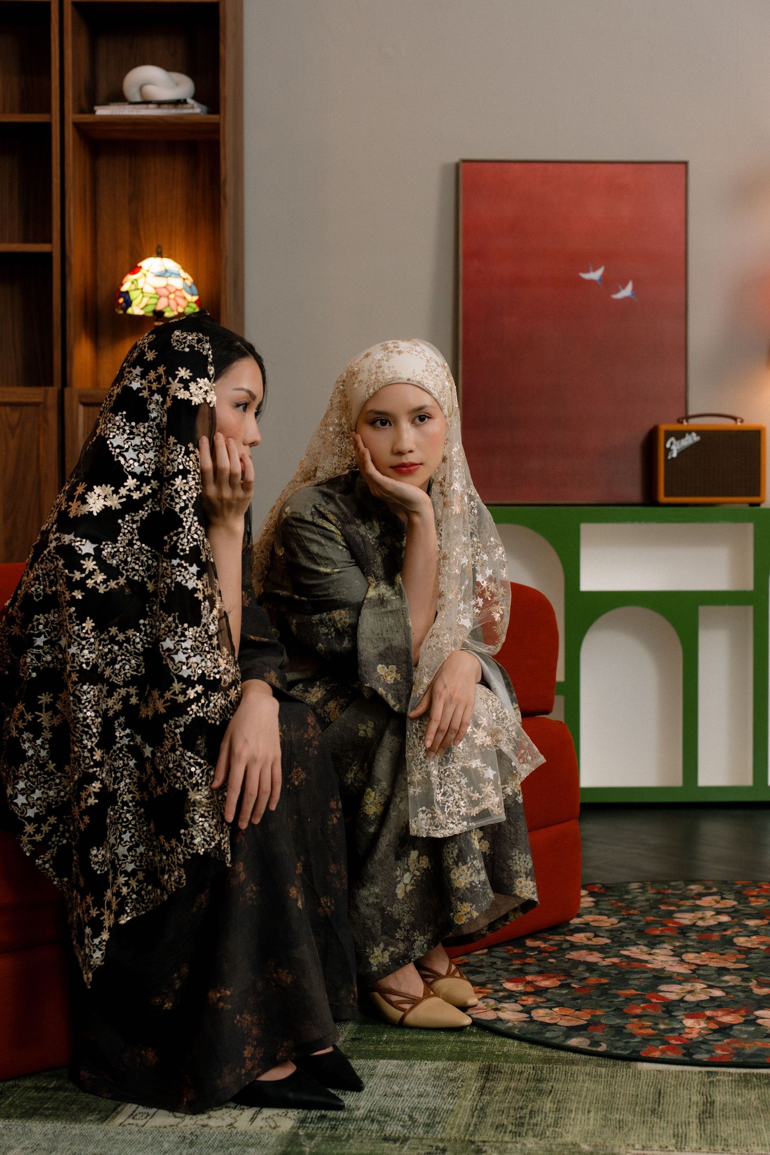 A sequence of artistic portraits showing two people in dark floral and lace clothing sitting against a wall with shelves.