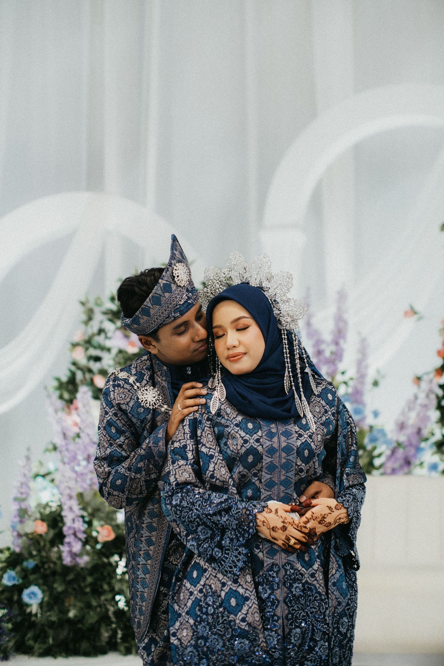 A mother and child wearing matching blue patterned outfits embrace in a garden setting with floral decorations.