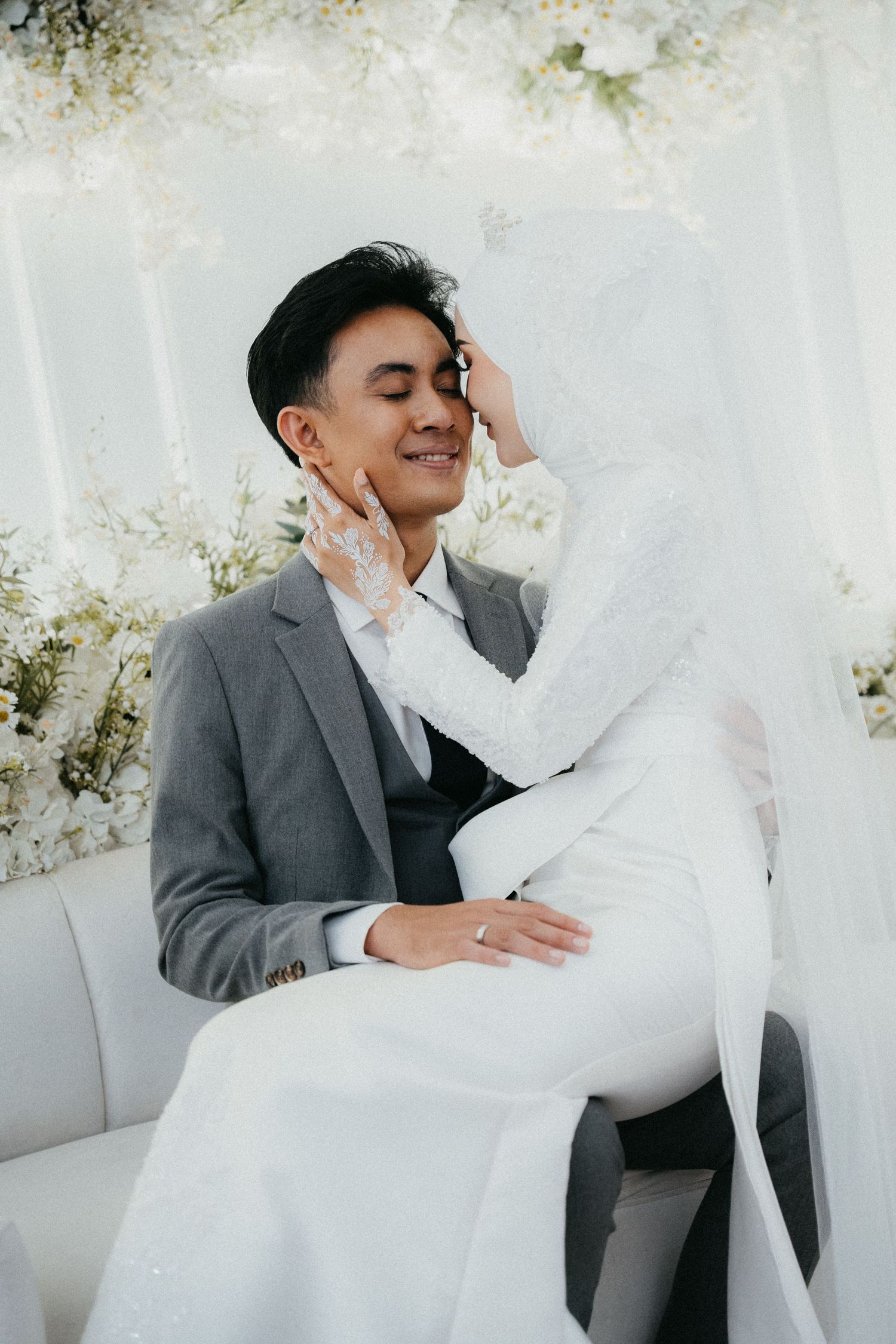 A tender moment in an elegant wedding photoshoot with the couple against a white background wearing gray and white attire.