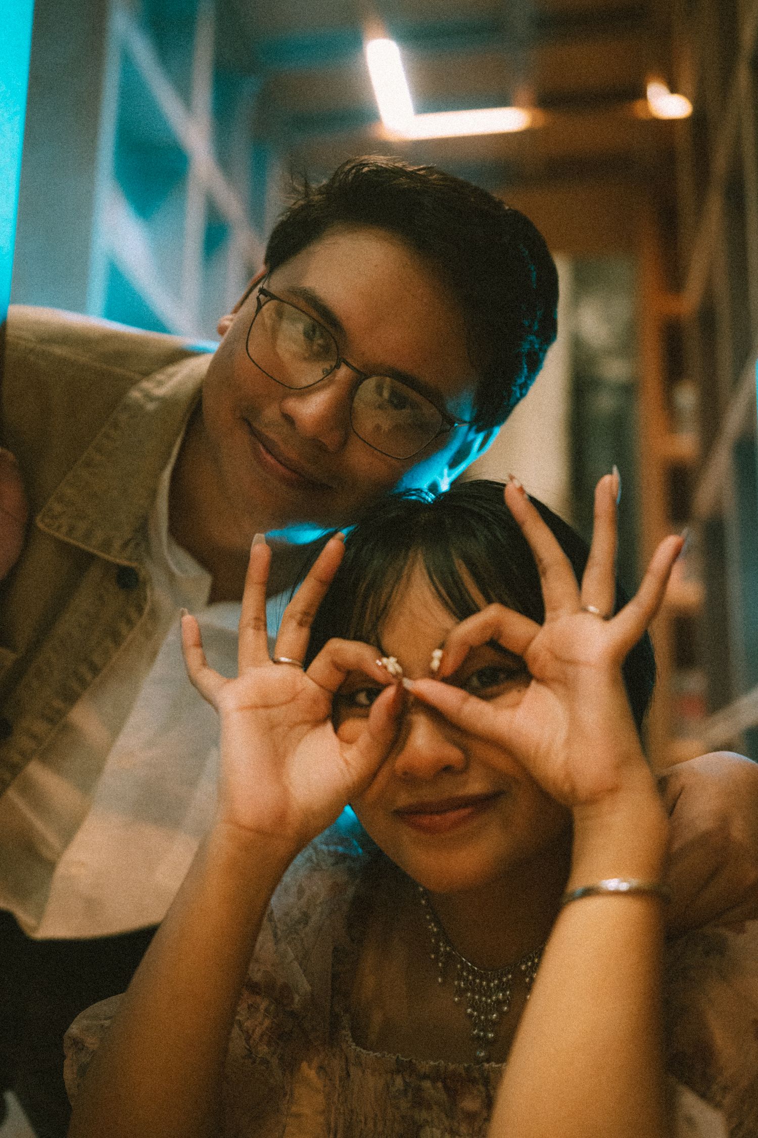 Playful moment captured in warm lighting as couple makes hand gestures near their eyes.