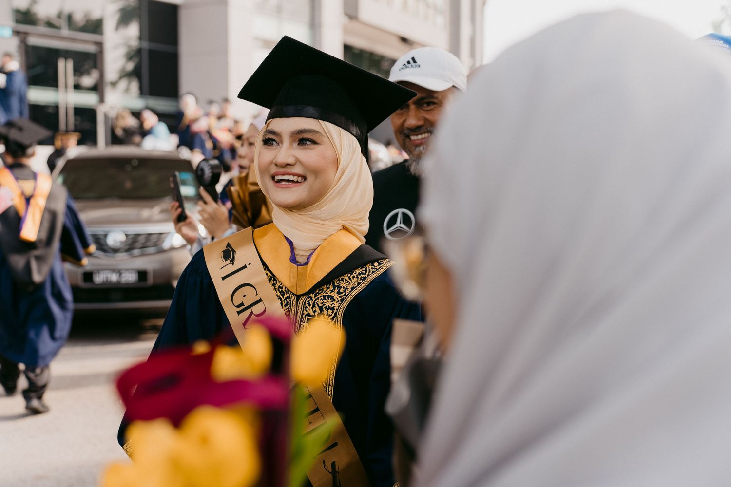 Graduate in black cap and gown celebrates with fellow graduates during outdoor commencement ceremony.