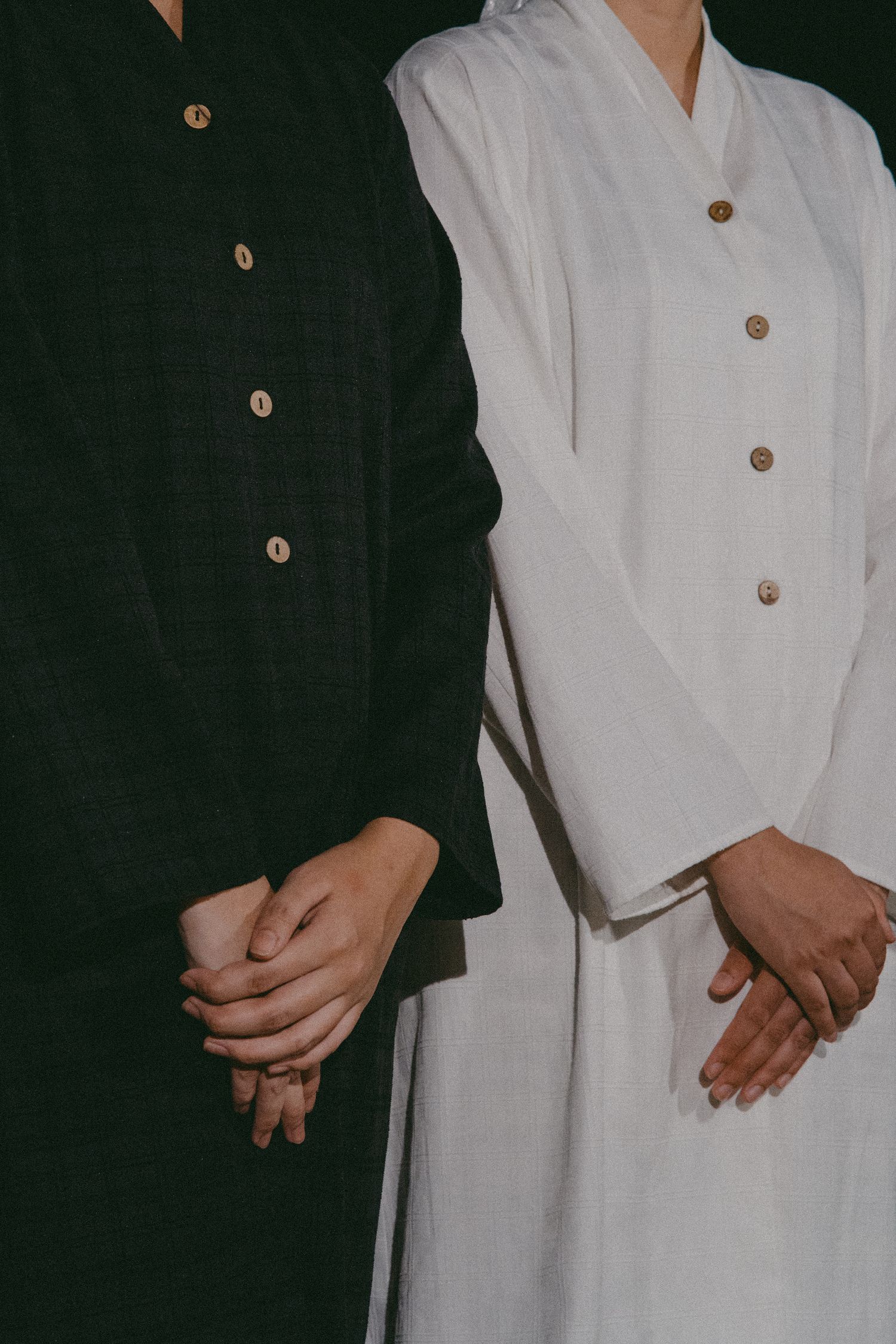 Close-up of two people standing side by side in contrasting black and white button-up garments.