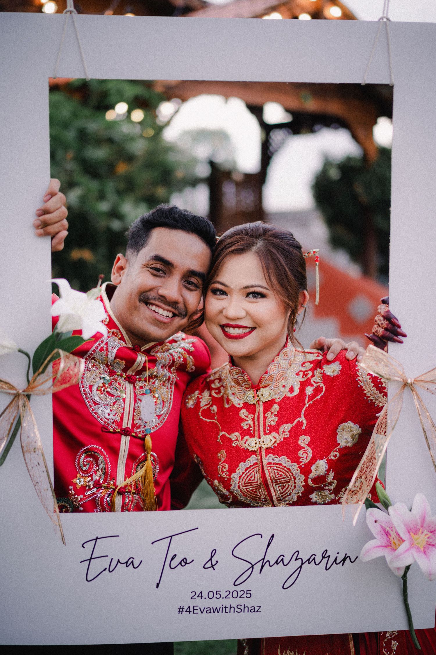 Two people wearing red traditional Chinese wedding attire pose together outdoors with decorative frames and lanterns.
