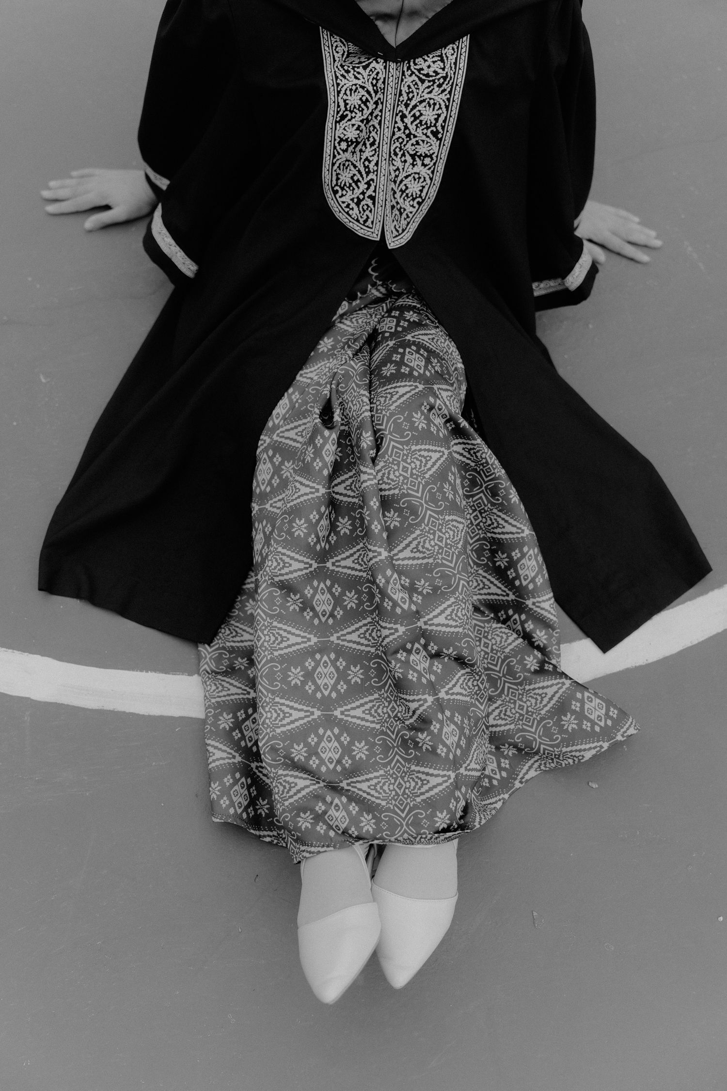 Black and white photo of a dress outfit featuring a dark blazer, patterned skirt, and white shoes laid flat.