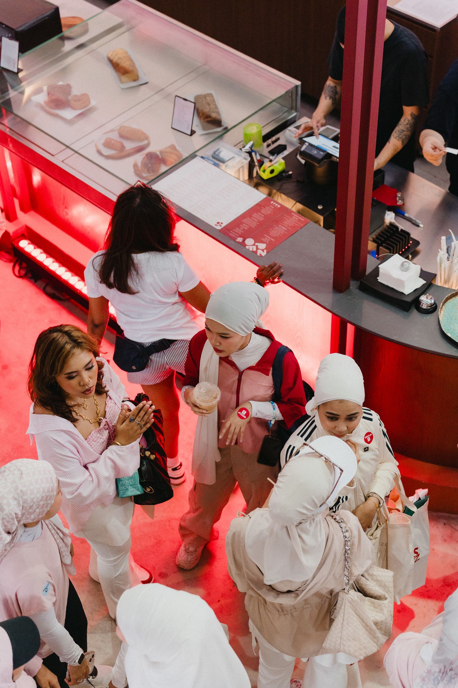 People in white uniforms and chef hats gather around a food service counter with red lighting below.