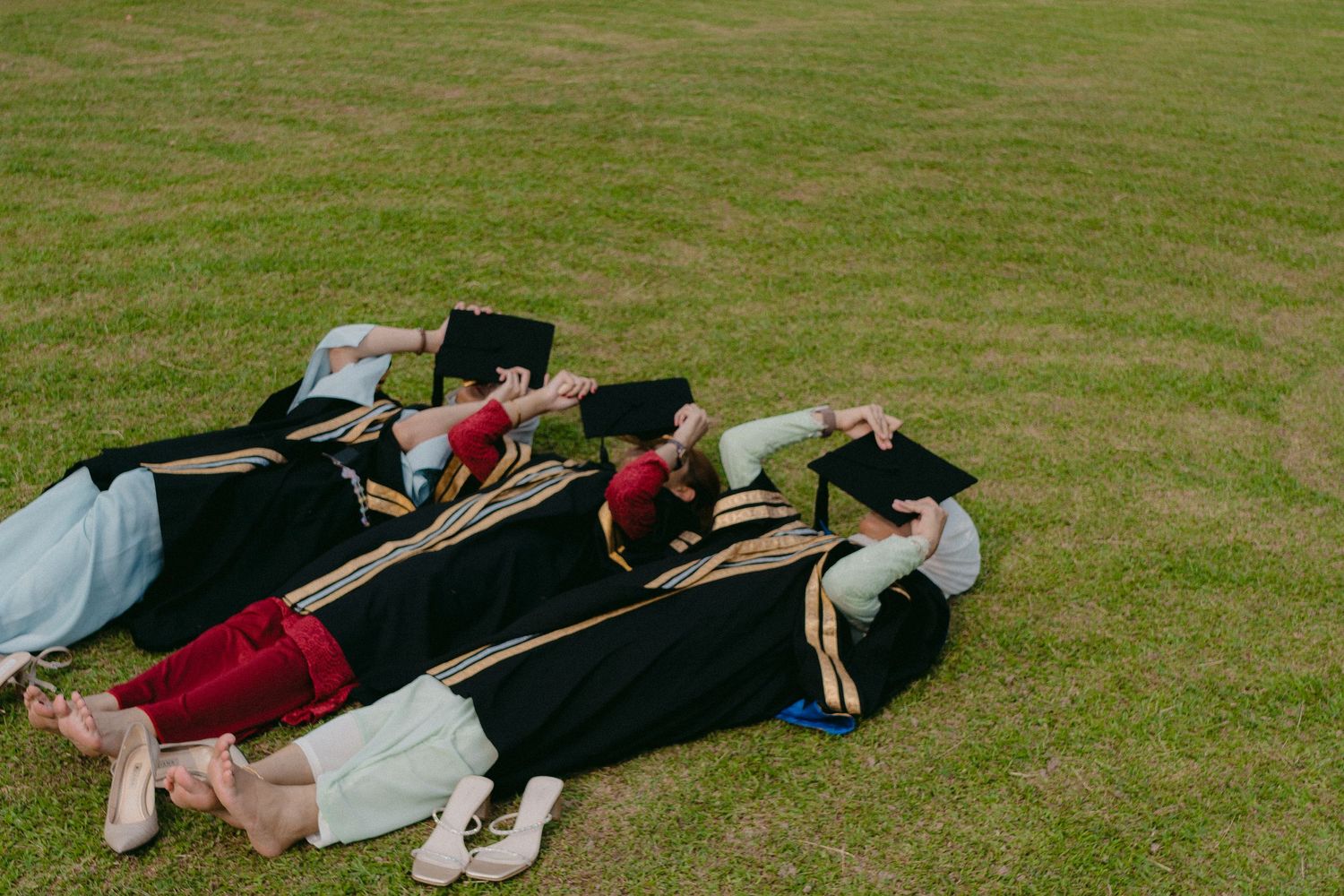 Graduates lying on grass having fun taking creative graduation photos together.