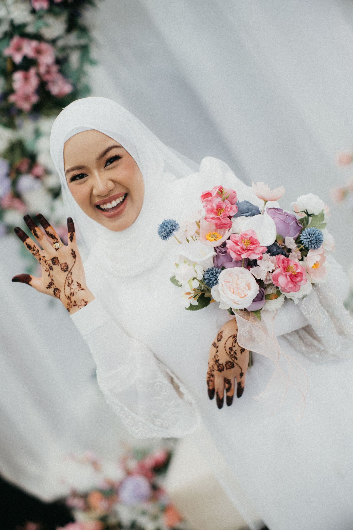Traditional bridal portraits featuring henna-decorated hands with pink and blue floral arrangements against soft light background.