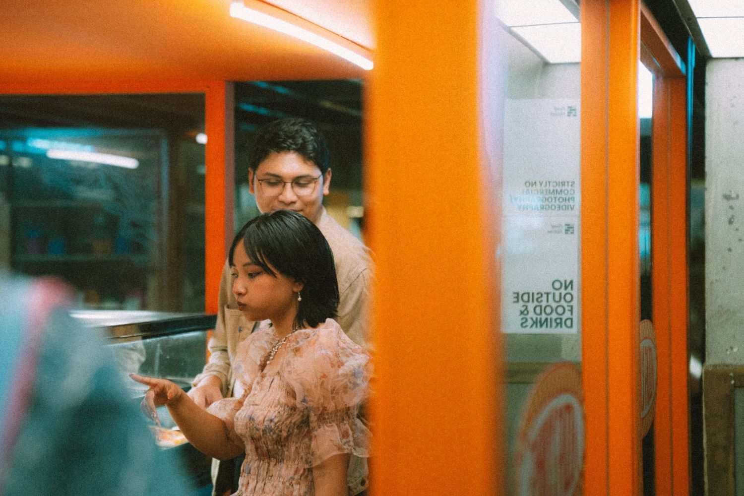 Couple standing close together in an orange-tinted subway or train station.