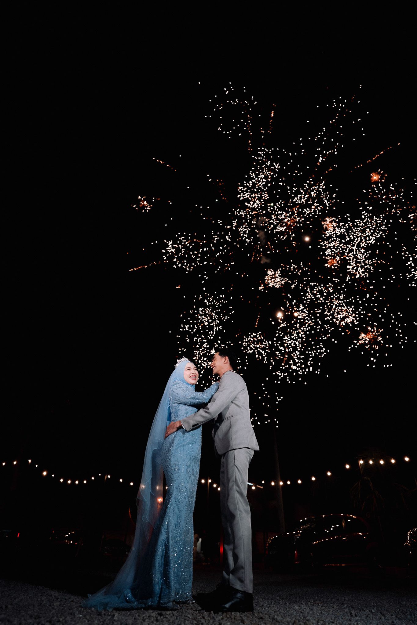 Muslim bride and groom embracing under spectacular fireworks display at outdoor night wedding celebration.