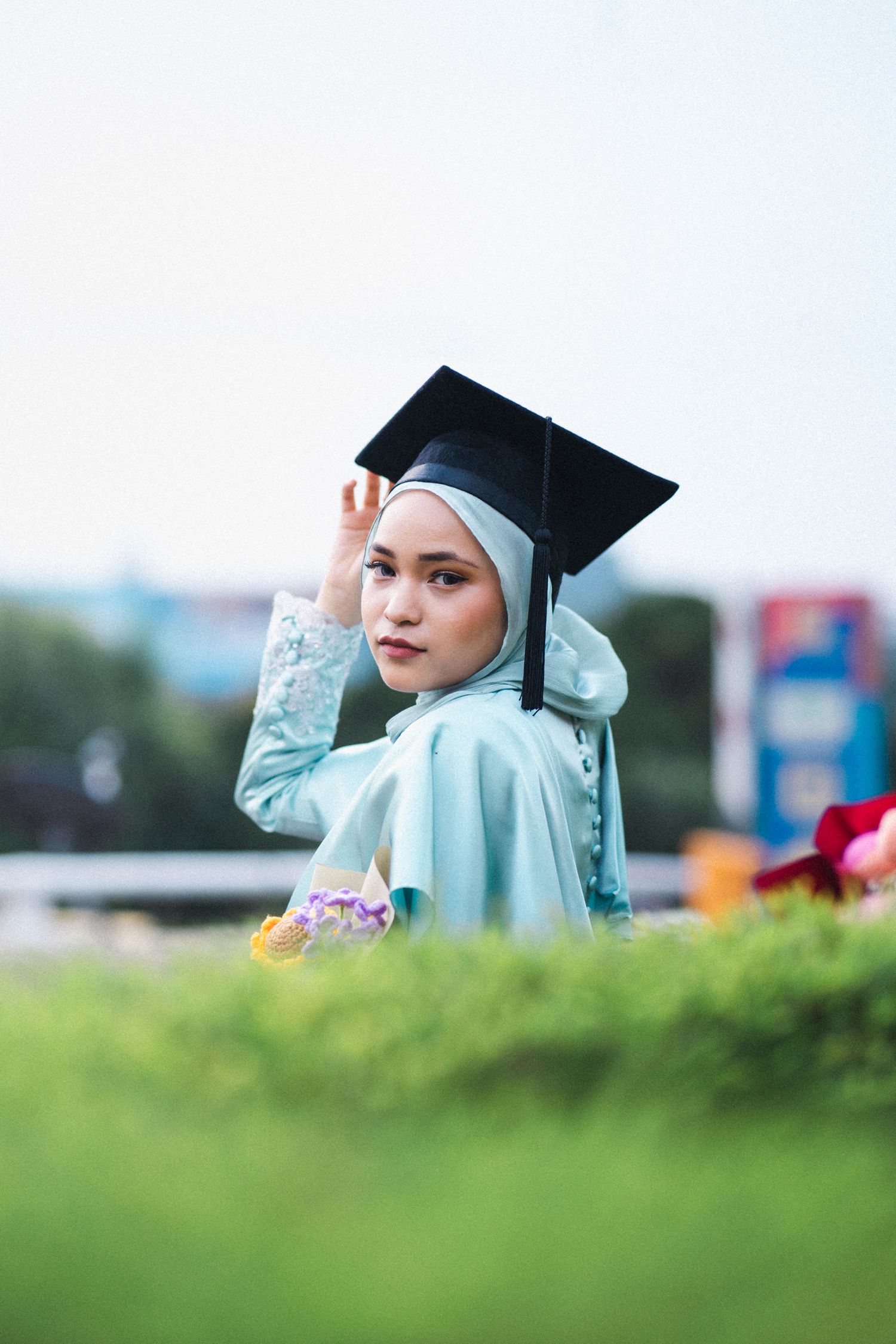 Graduate in mint green dress and black cap poses against blurred natural background.