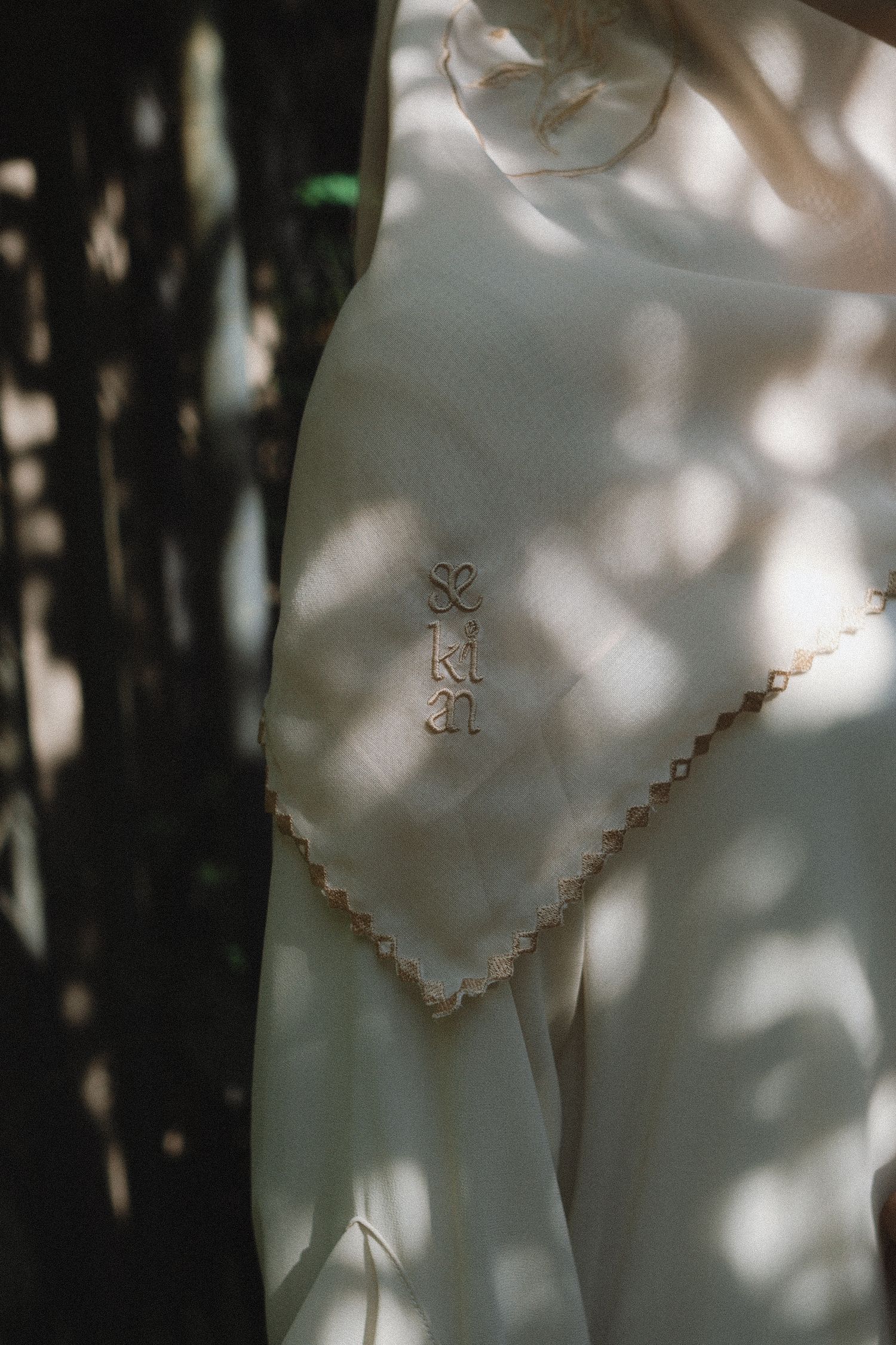 Close-up of white graduation dress fabric with delicate embroidered details in dappled sunlight.