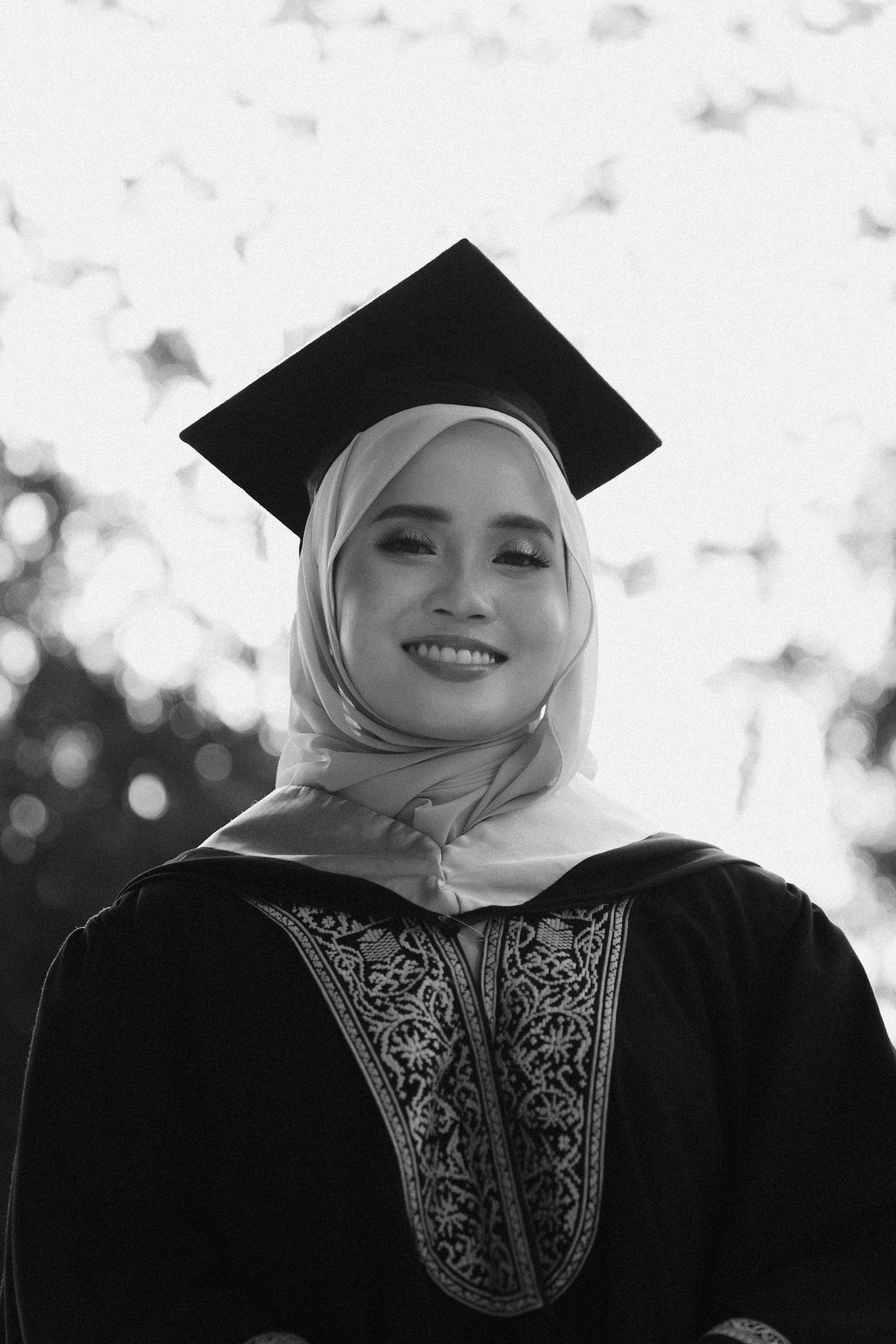 A graduate in traditional academic regalia and hijab poses for a series of black and white portraits.