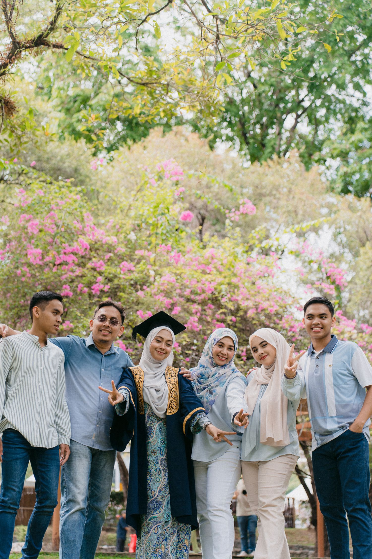 Group of friends celebrating outdoors under blooming trees with pink flowers in a park setting.