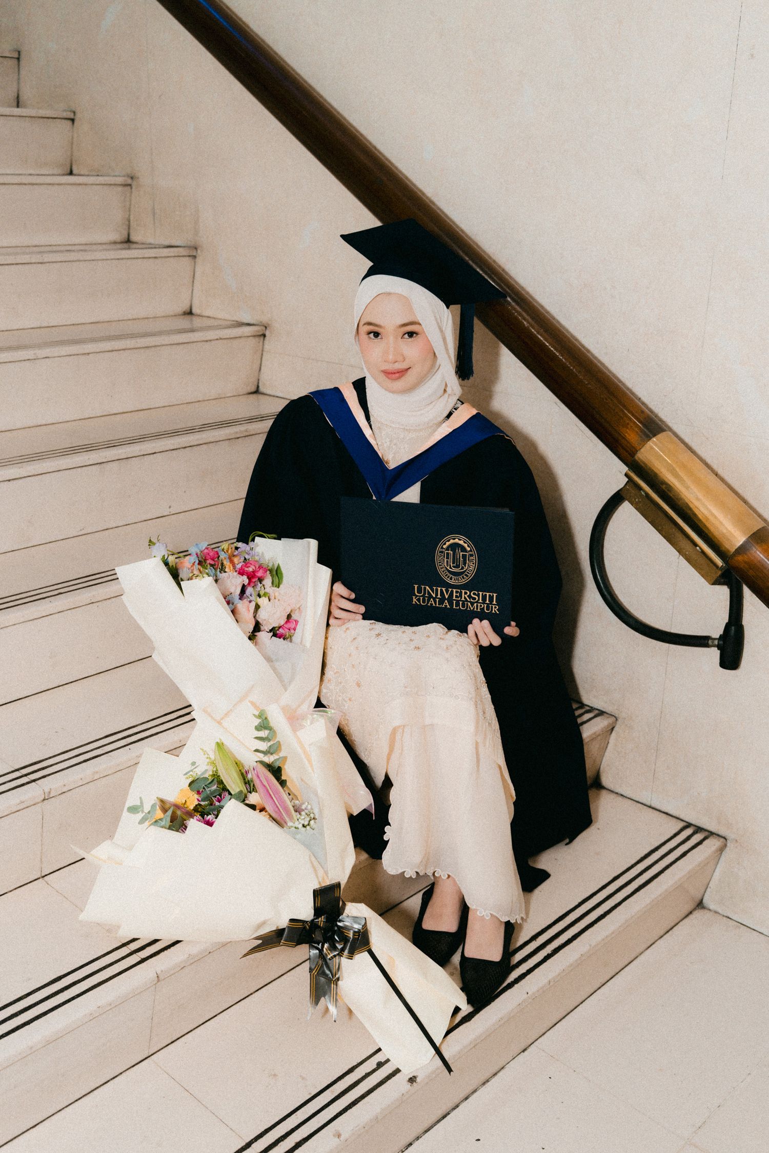 A person wearing a hijab and navy sweater sits on white stairs in a minimalist setting.