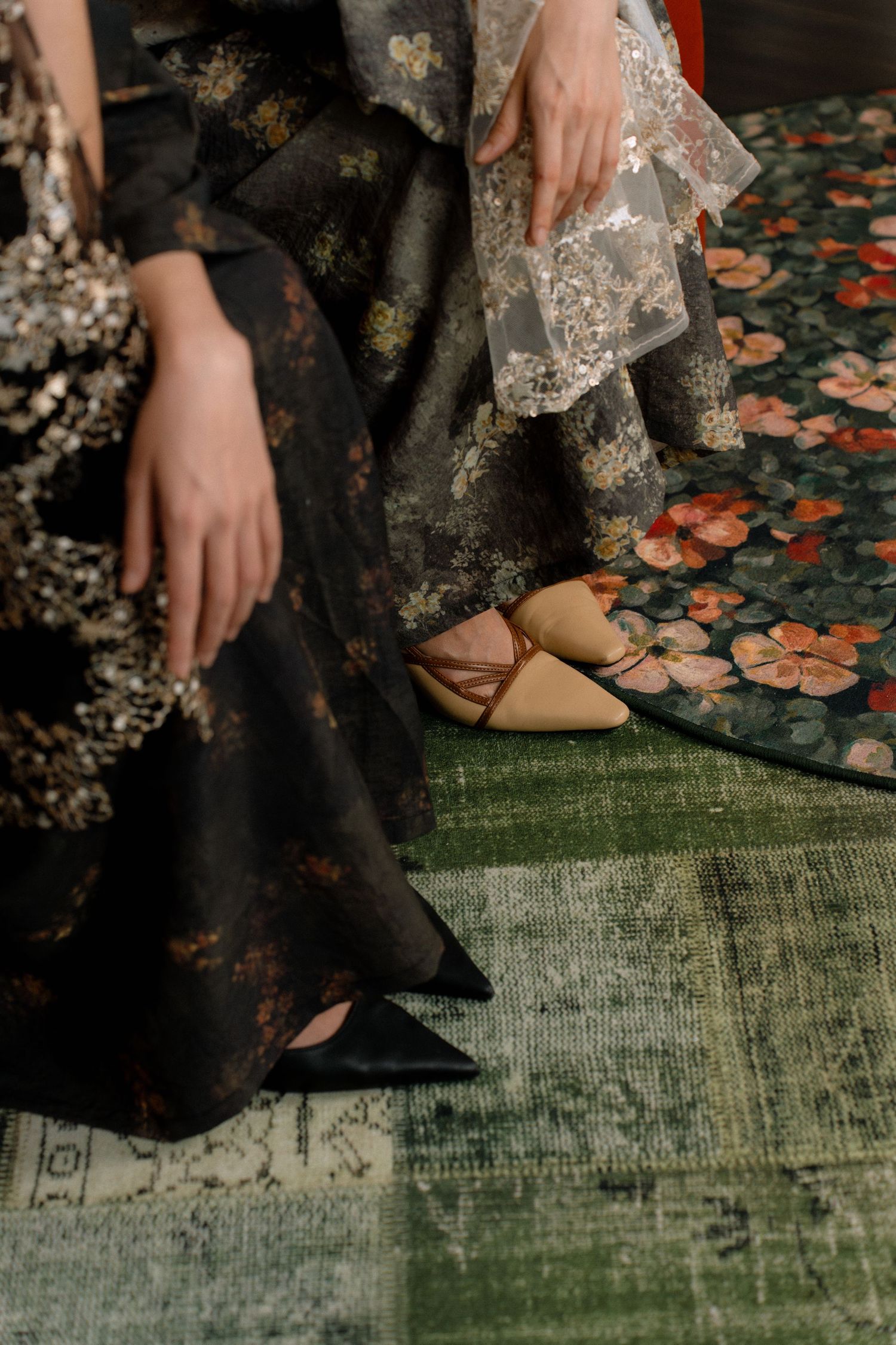 Elegant floral dress with lace details and beige slippers rests against a vintage floral carpet and green rug.