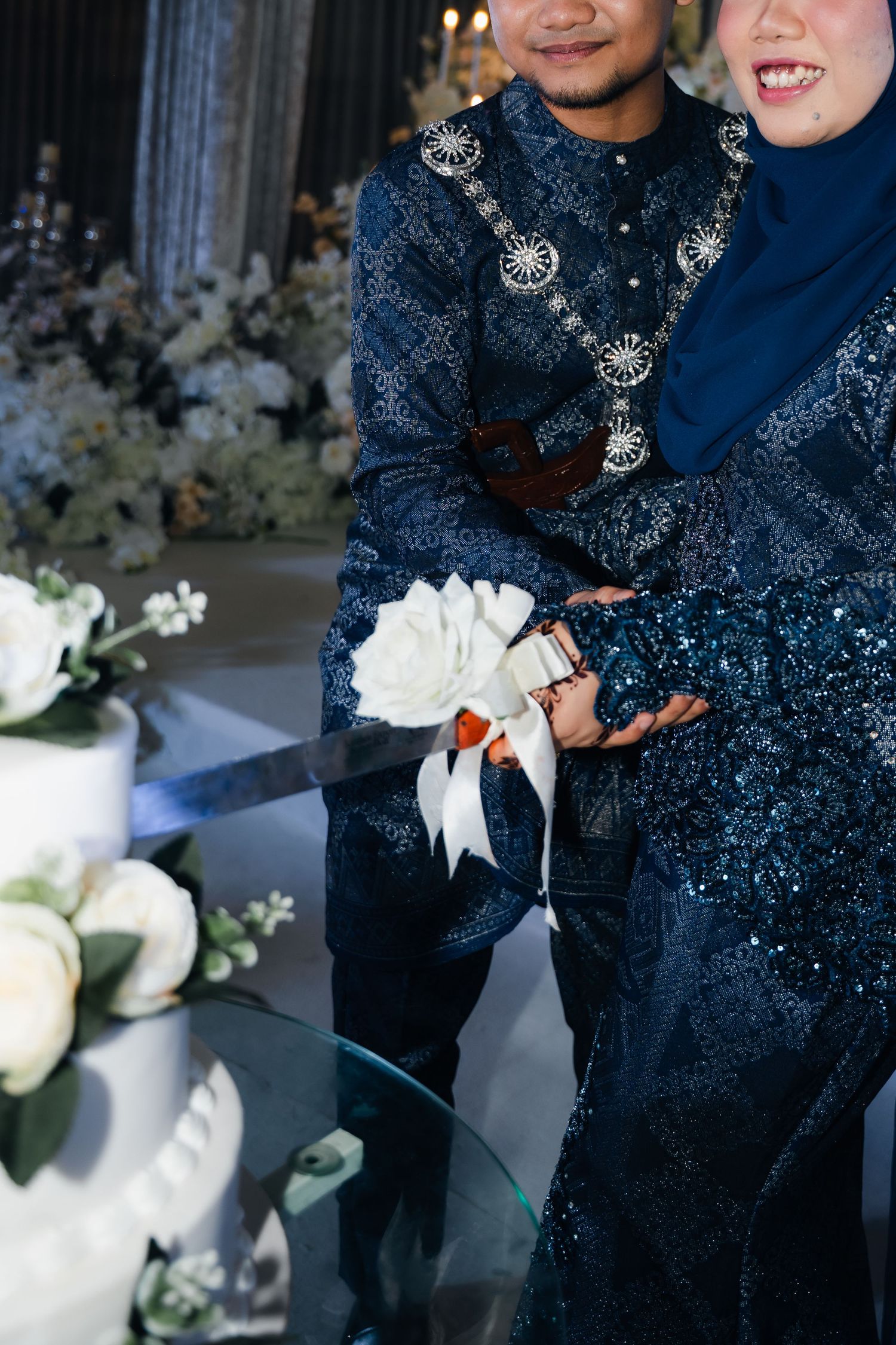 Wedding couple in traditional navy sequined attire holding white bouquet during evening celebration ceremony.