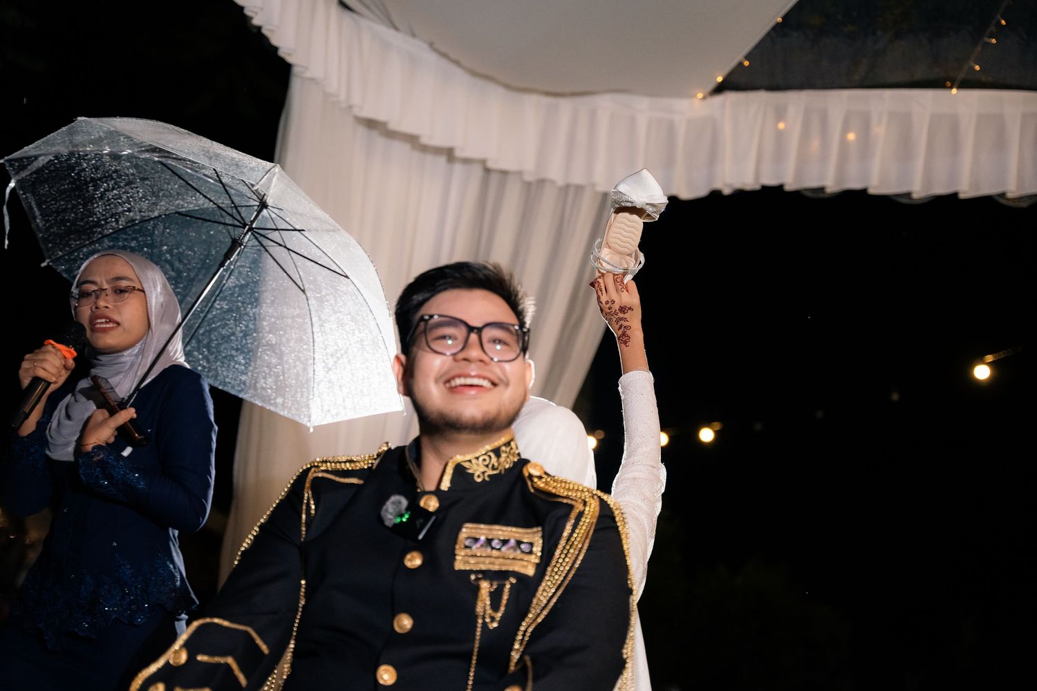 Wedding party holding white umbrellas stands outside at night while being illuminated by off-camera lighting.