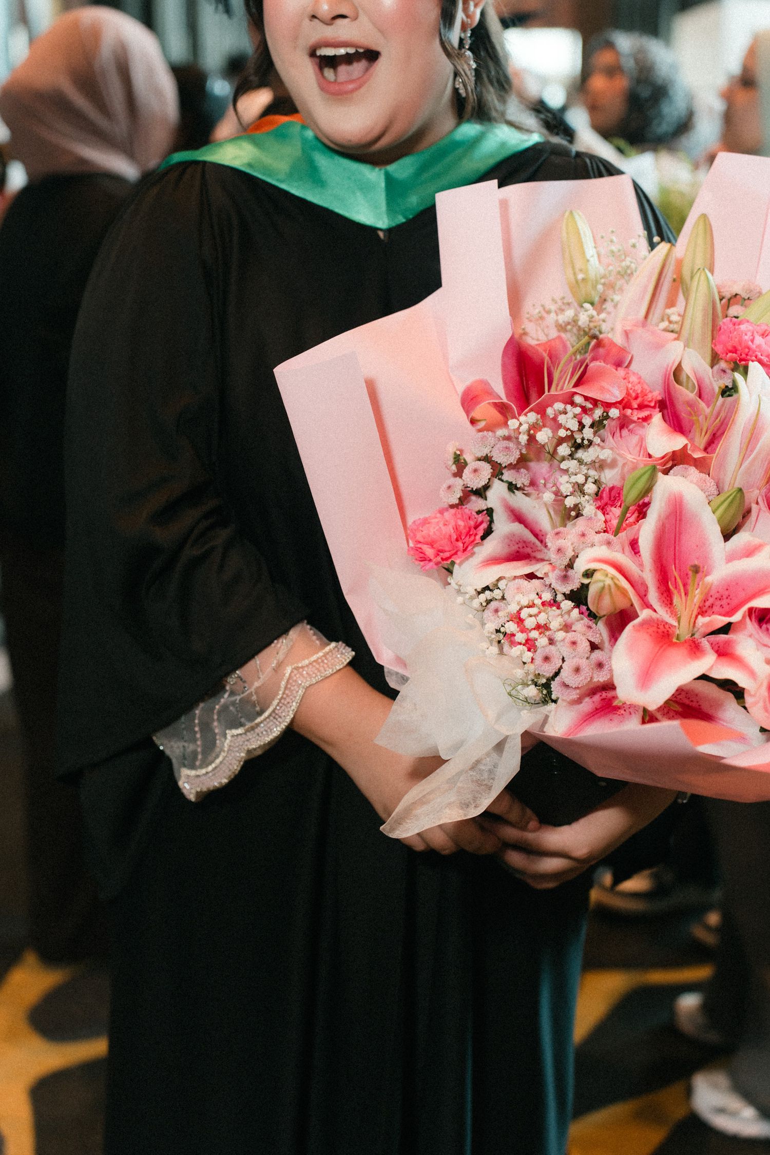 A row of people holding pink floral bouquets with lilies and delicate tissue paper wrapping at a formal event.