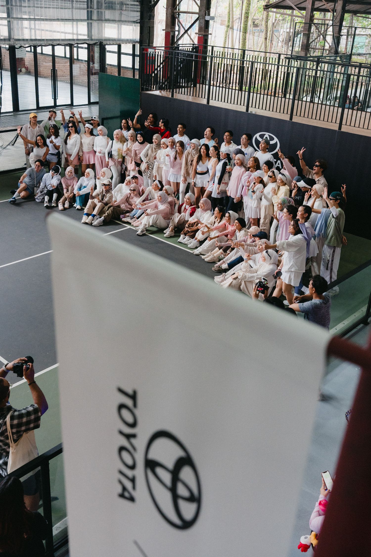 A large group of people in white and light colored clothing seated in bleachers at an indoor sports facility.