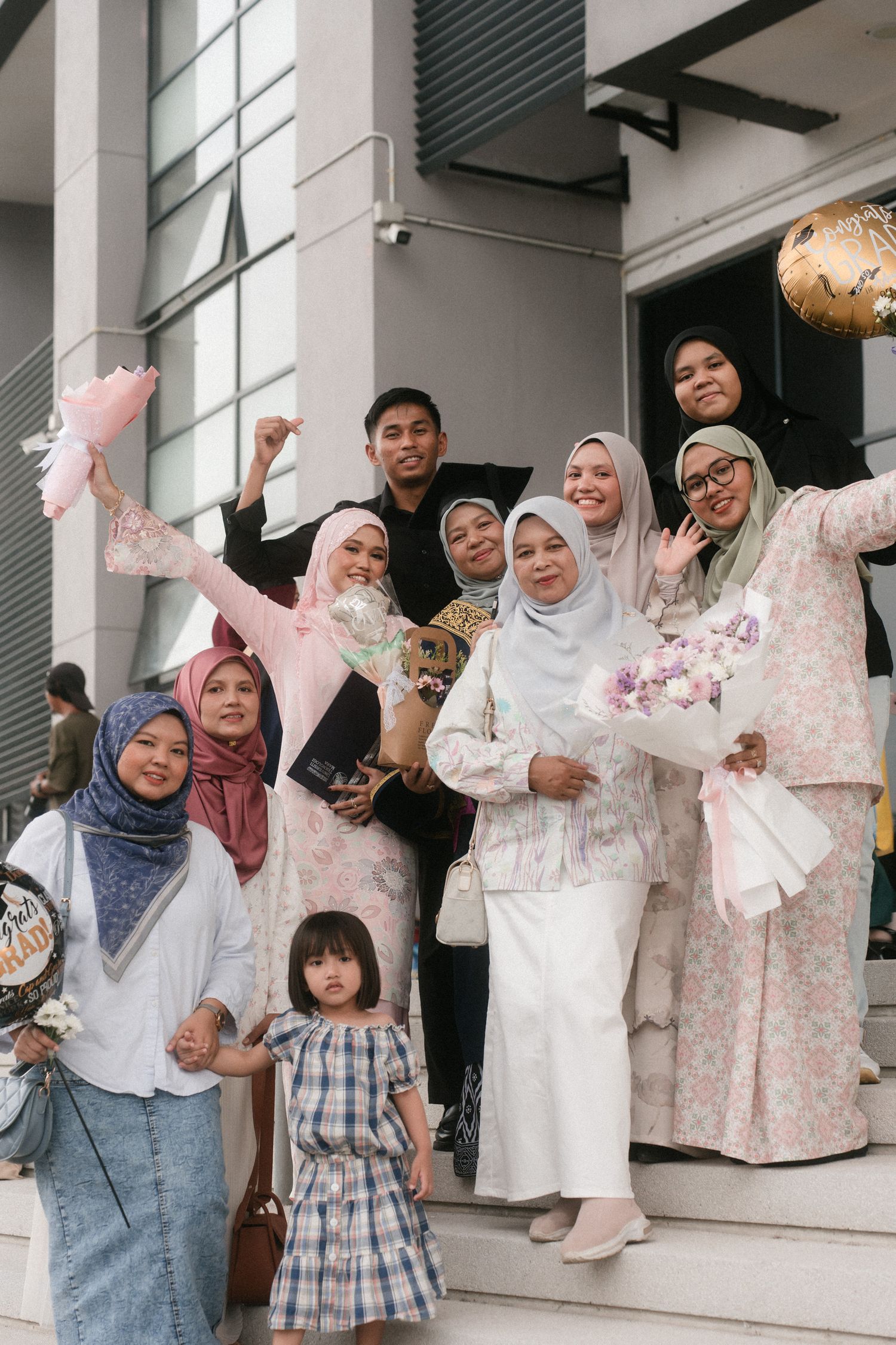 A group of people wearing matching floral outfits and hijabs pose together on a white porch.