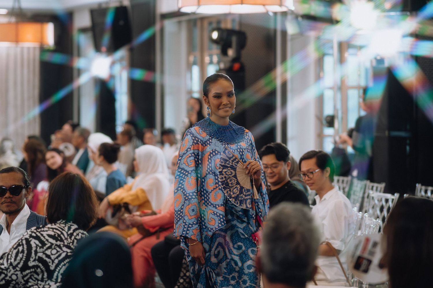 Fashion model walks runway in blue patterned dress at upscale fashion show event.