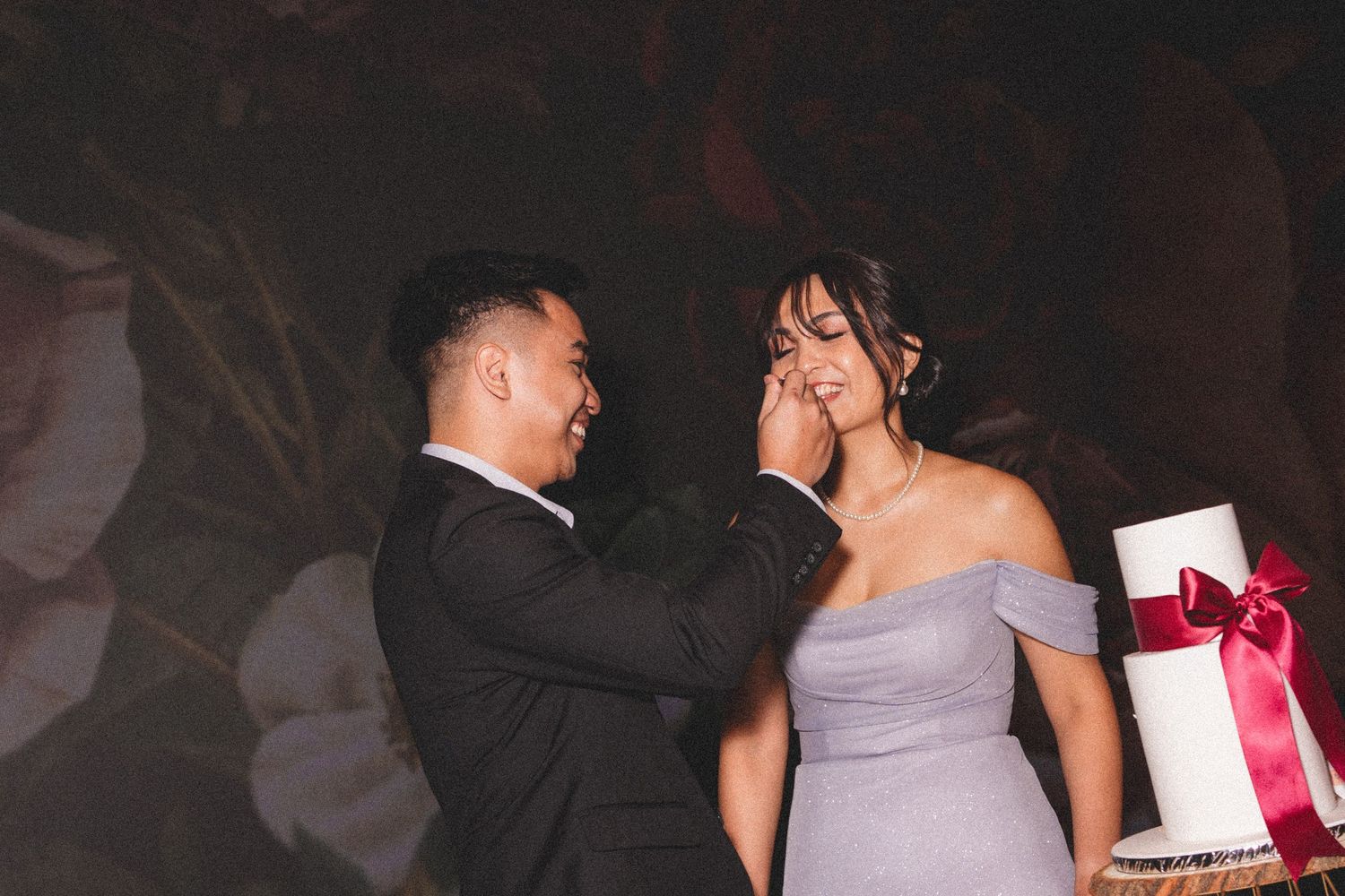 A couple in formal attire shares an emotional moment at a celebration with gifts visible in the background.