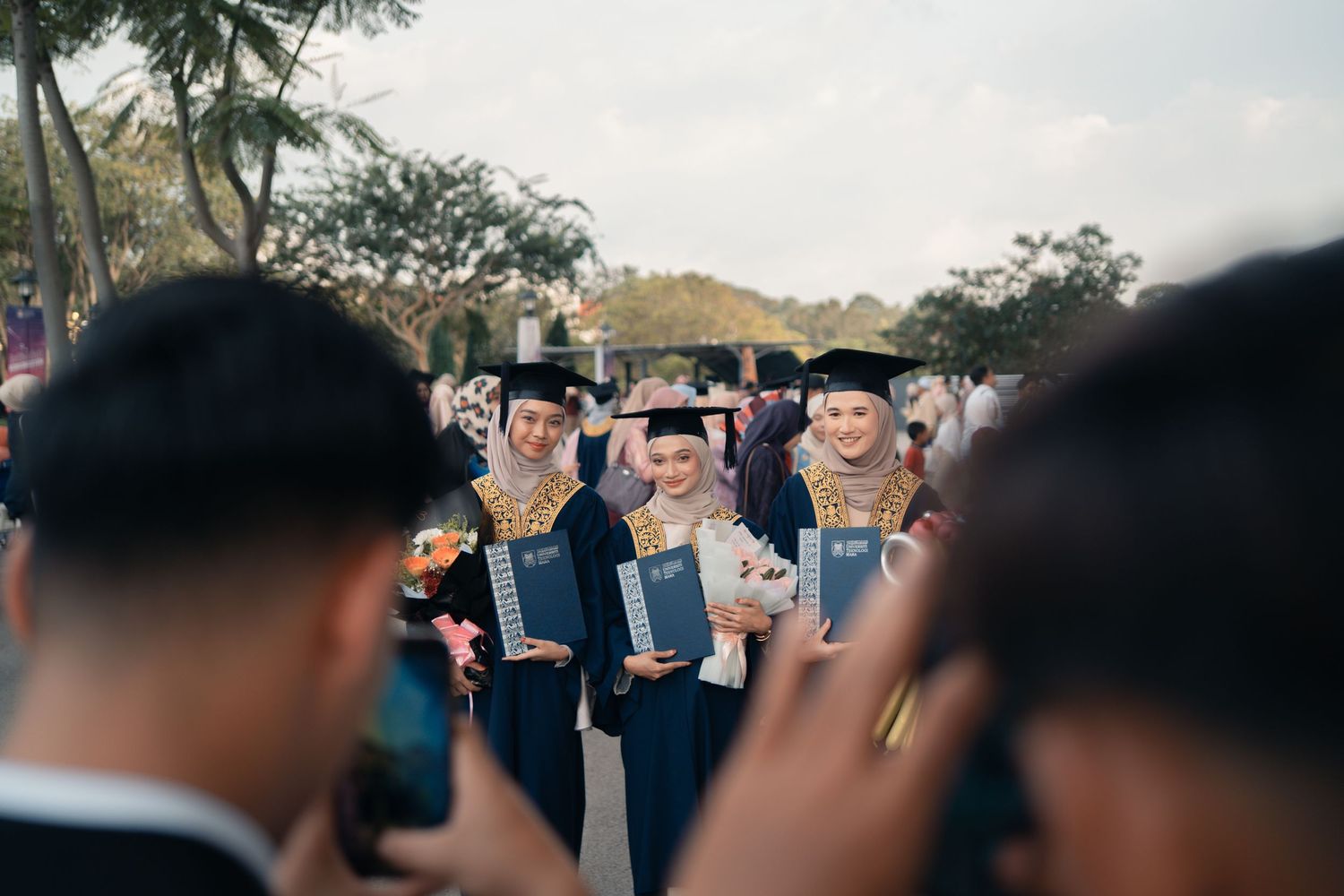 Group of graduates in blue gowns taking photos during commencement ceremony.
