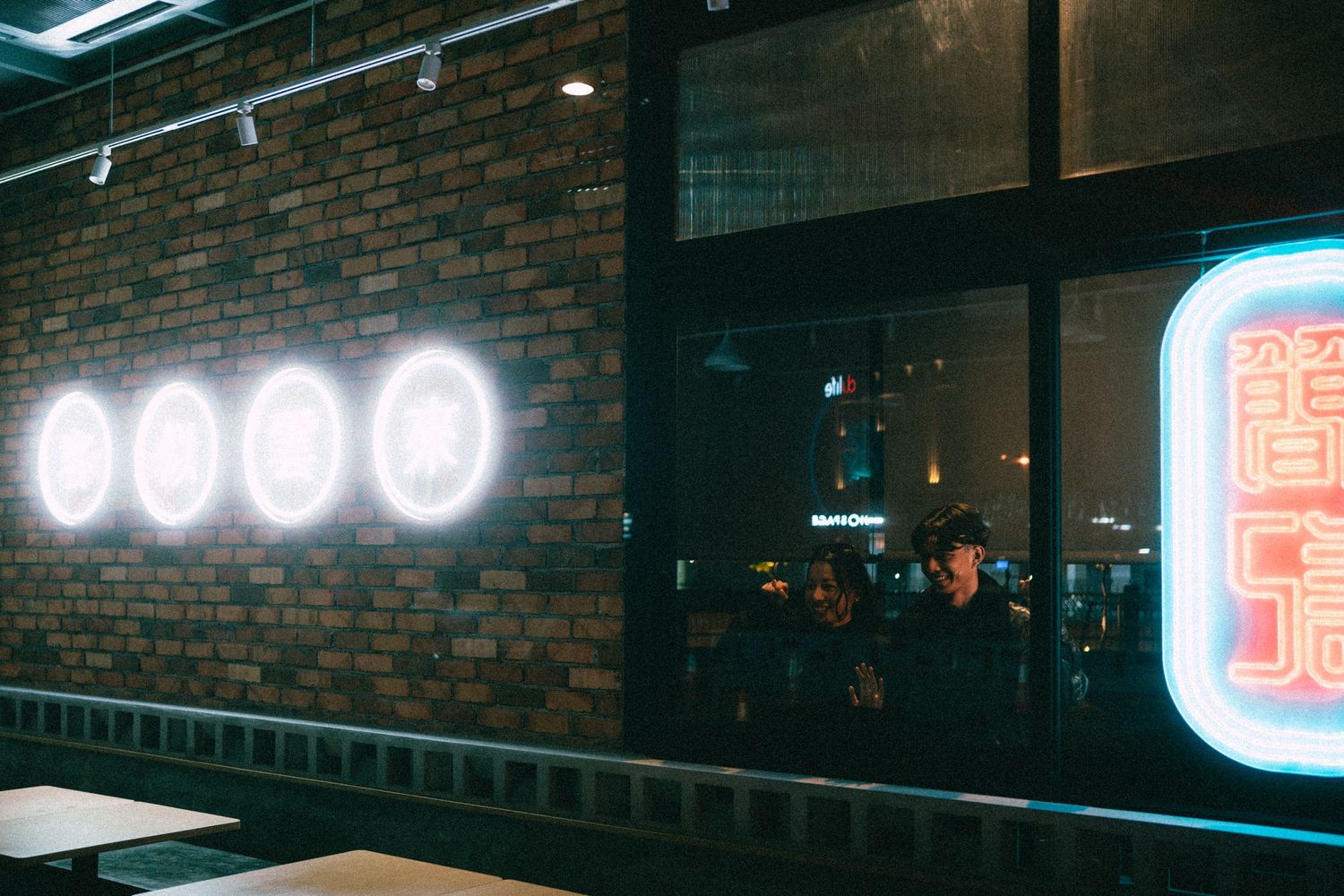 Neon lights glowing on a brick wall inside a moody urban restaurant or bar.