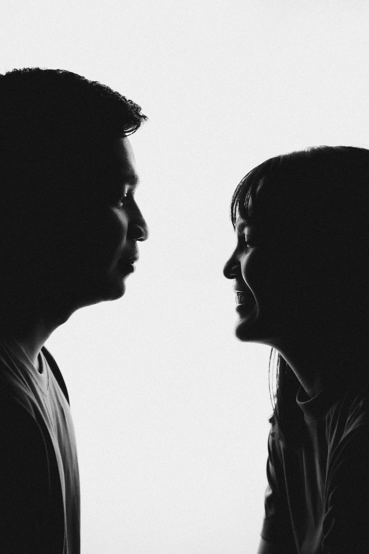 Dramatic black and white silhouette profile of two people facing each other against white background.