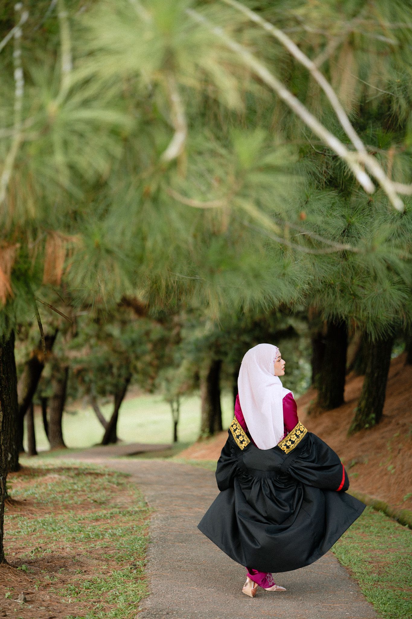 Muslim woman in black abaya and white hijab walking on a serene tree-lined park path.