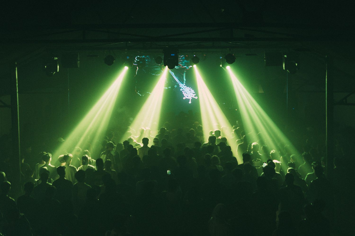 Green stage lights illuminate a dark concert venue filled with silhouetted crowd members.