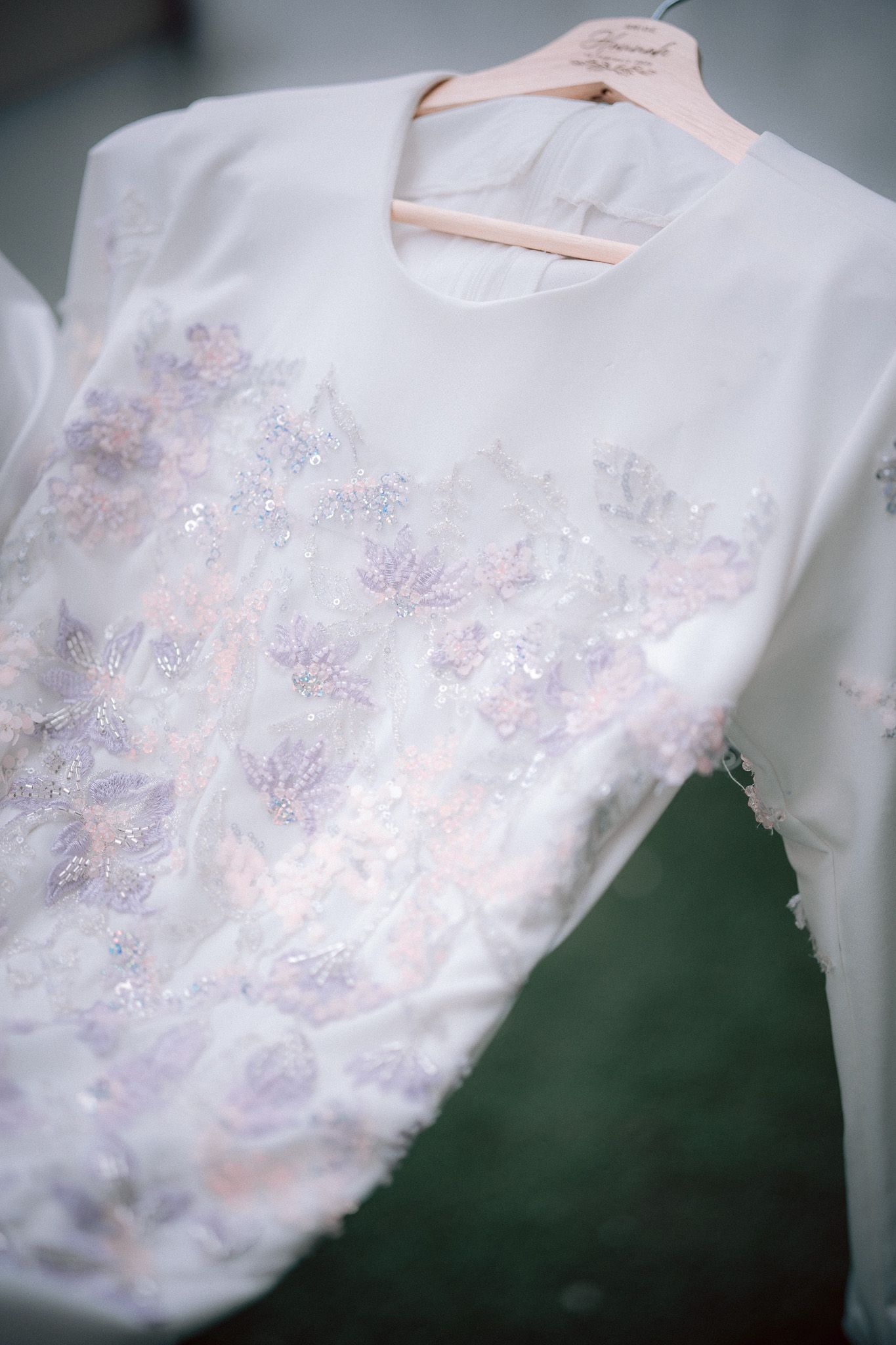 White bridal top with delicate floral lace embroidery and sequin details hanging on a wooden hanger.