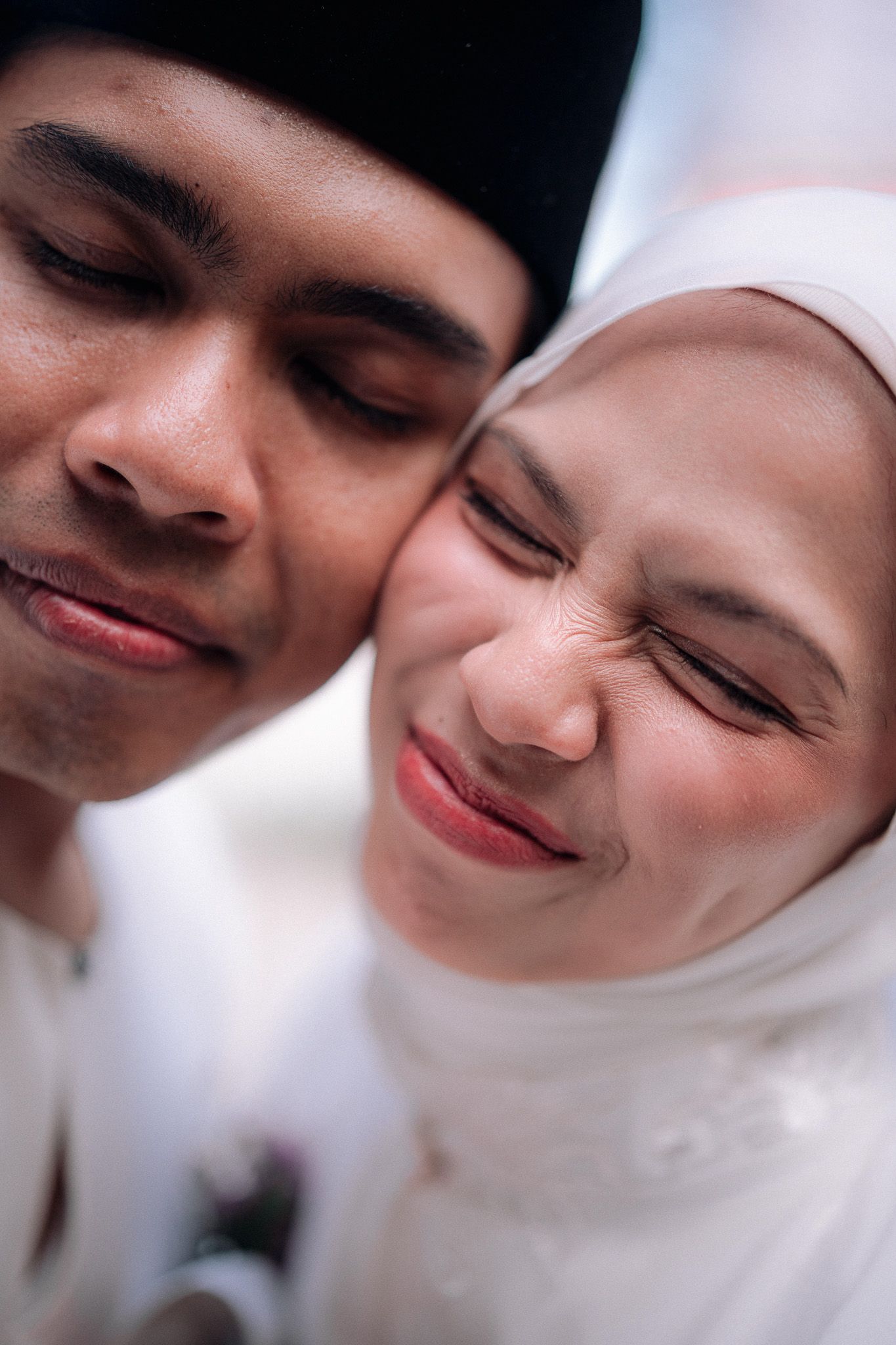 Close-up of Muslim bride and groom in white wedding attire sharing a tender moment.