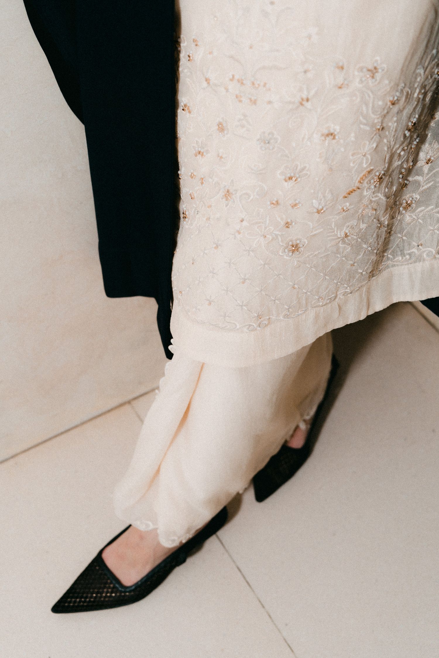 A close-up sequence showing the hem of a white lace wedding dress and black shoes against a light floor.