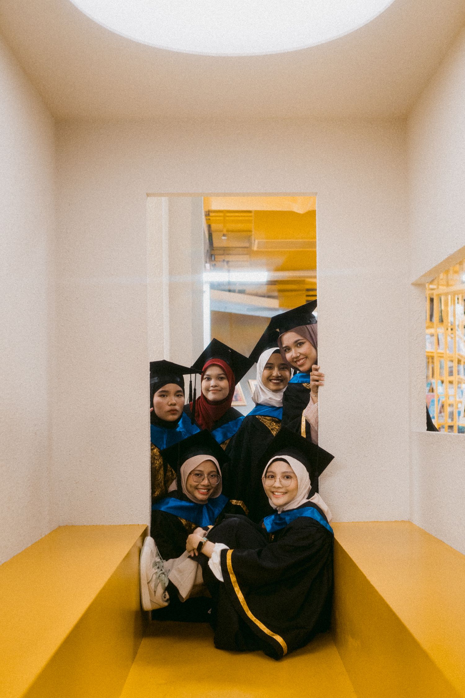 Graduates in black and blue robes pose together in a yellow-floored hallway.