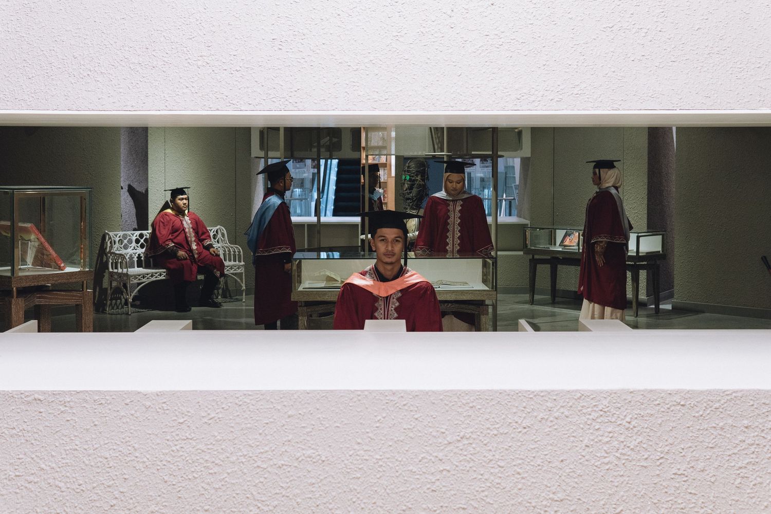 Graduate students in maroon gowns study in a modern library setting.