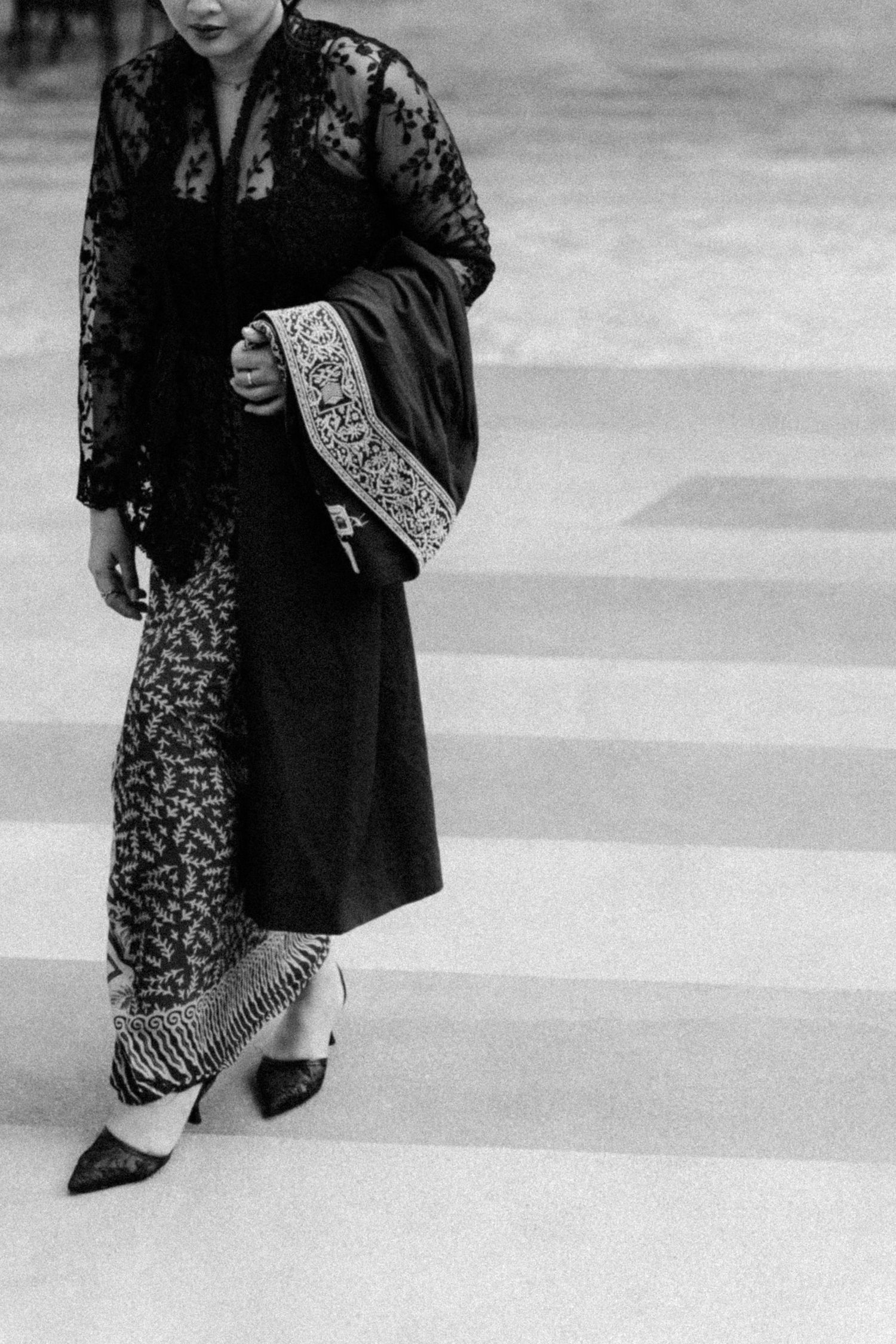 Black and white fashion photograph showing elegant lace jacket and patterned dress with ornate embroidered details.