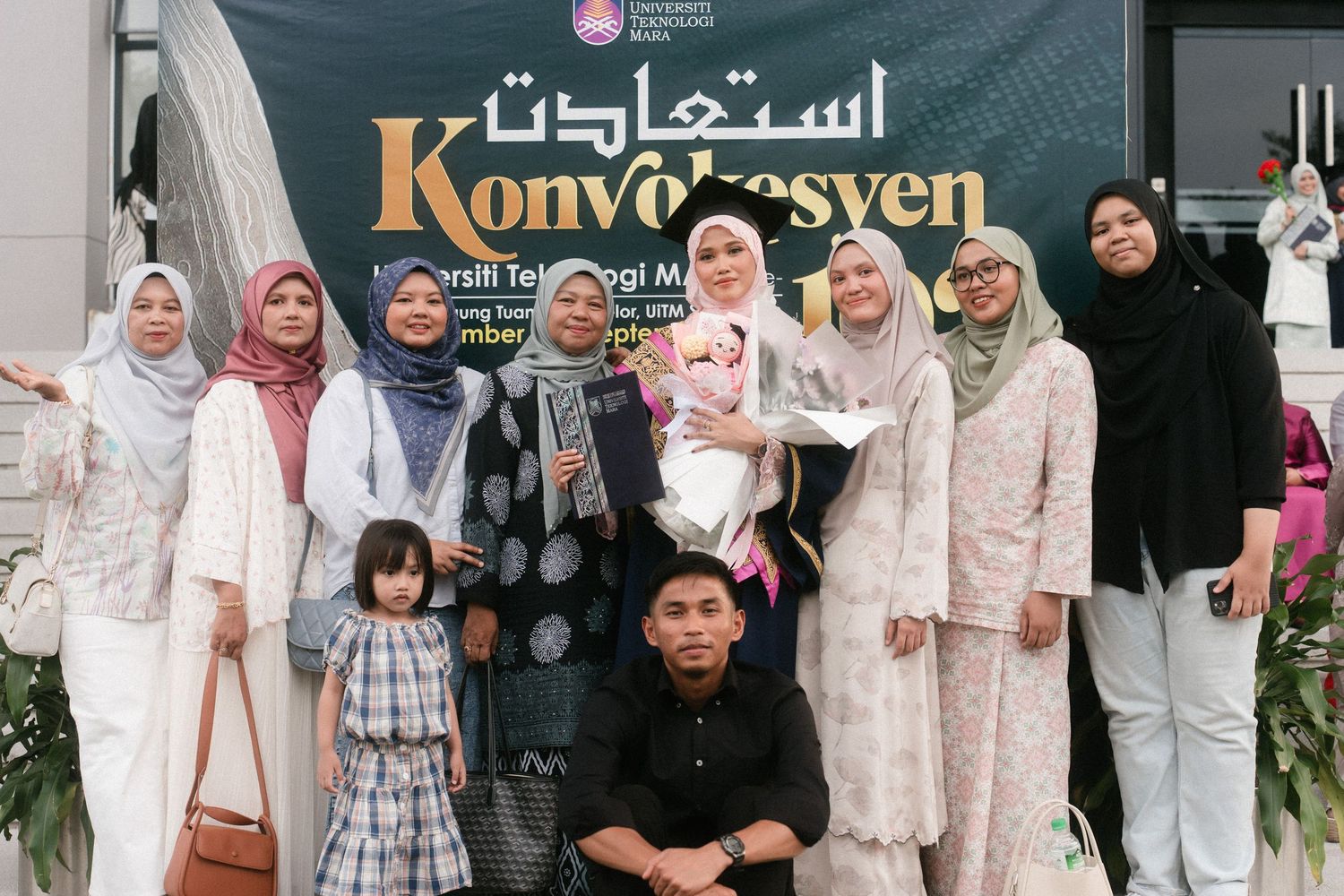 A group in light colored traditional clothing poses together in front of a Konvekyen storefront sign.