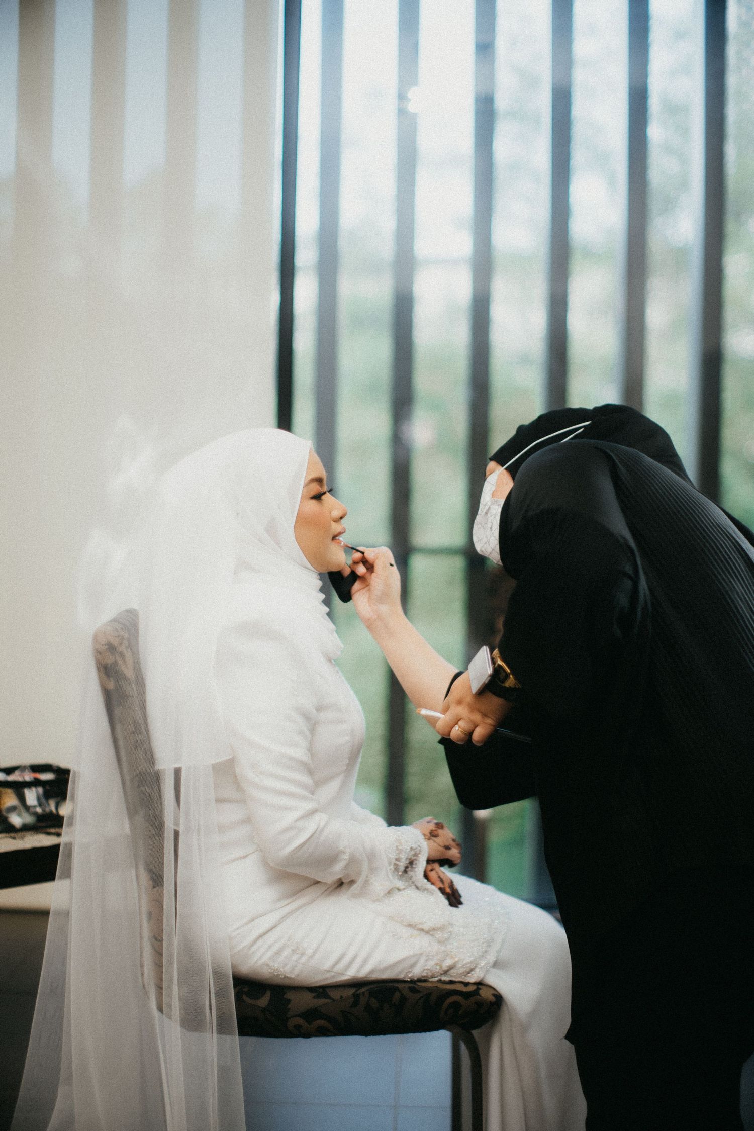 Three women in white hijabs and traditional clothing sit near a large window in a modern interior setting.