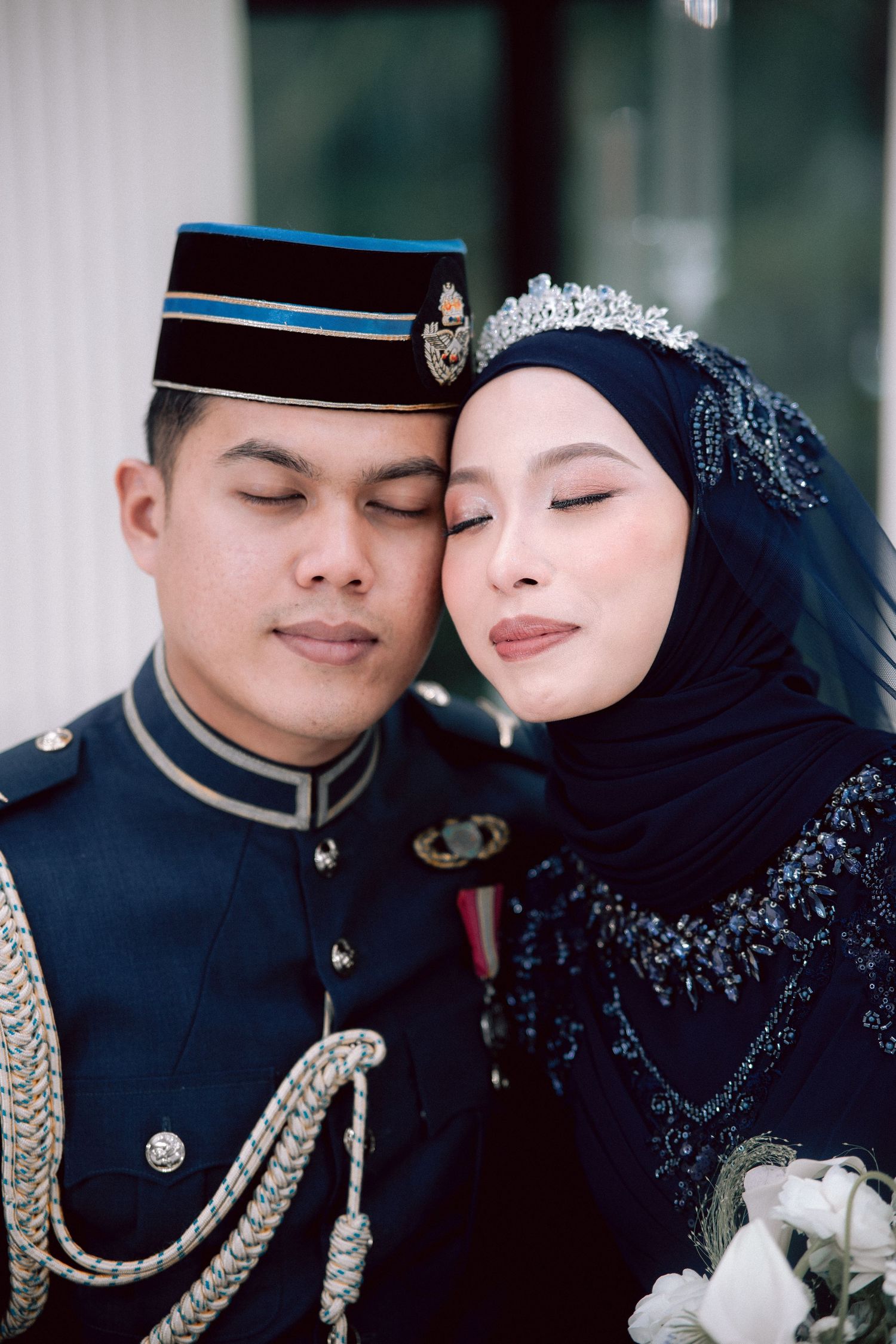 A romantic wedding portrait showing a couple in traditional Malaysian military dress and hijab with floral accents.